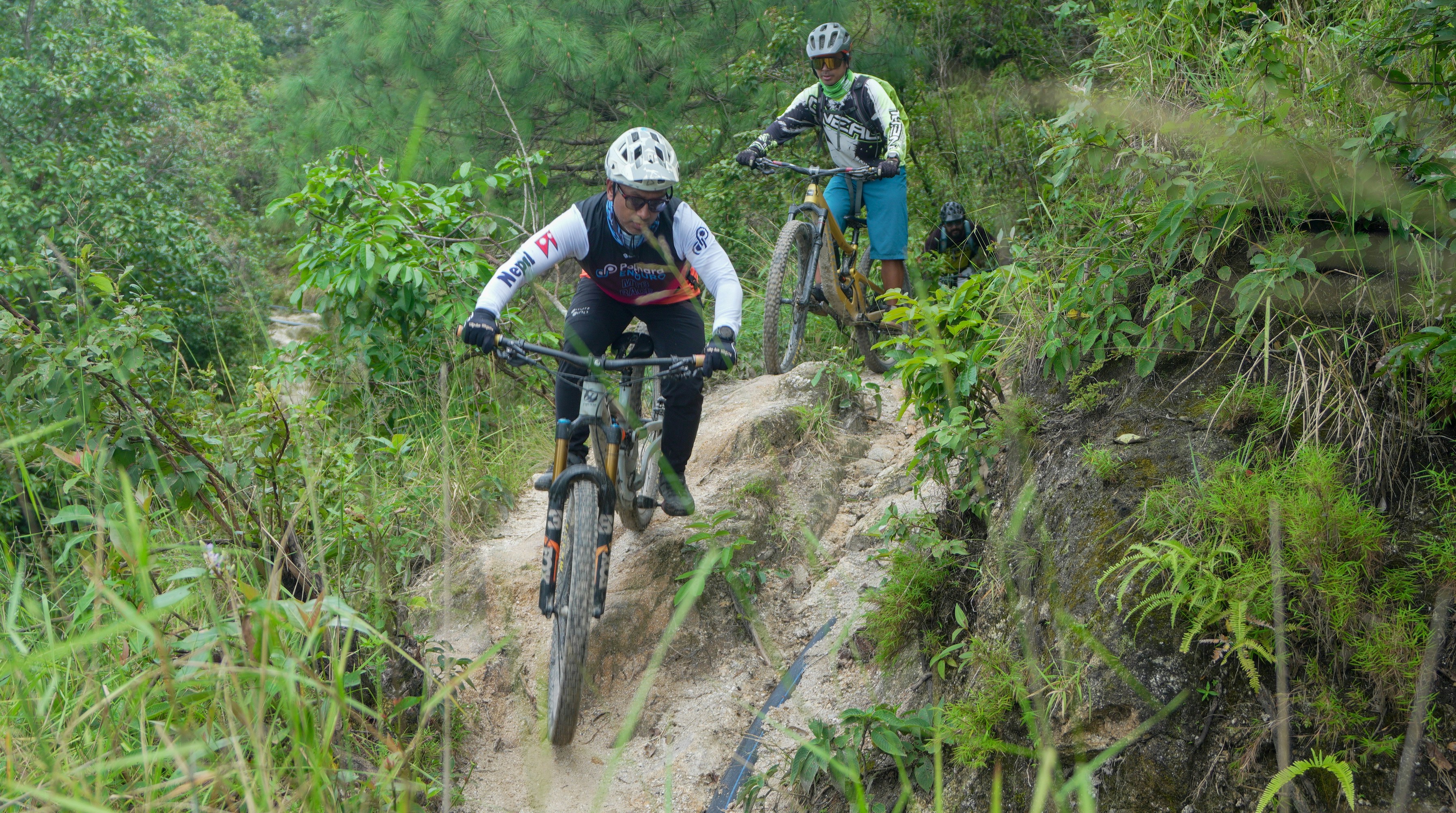 Two people mountain biking on a dirt trail.