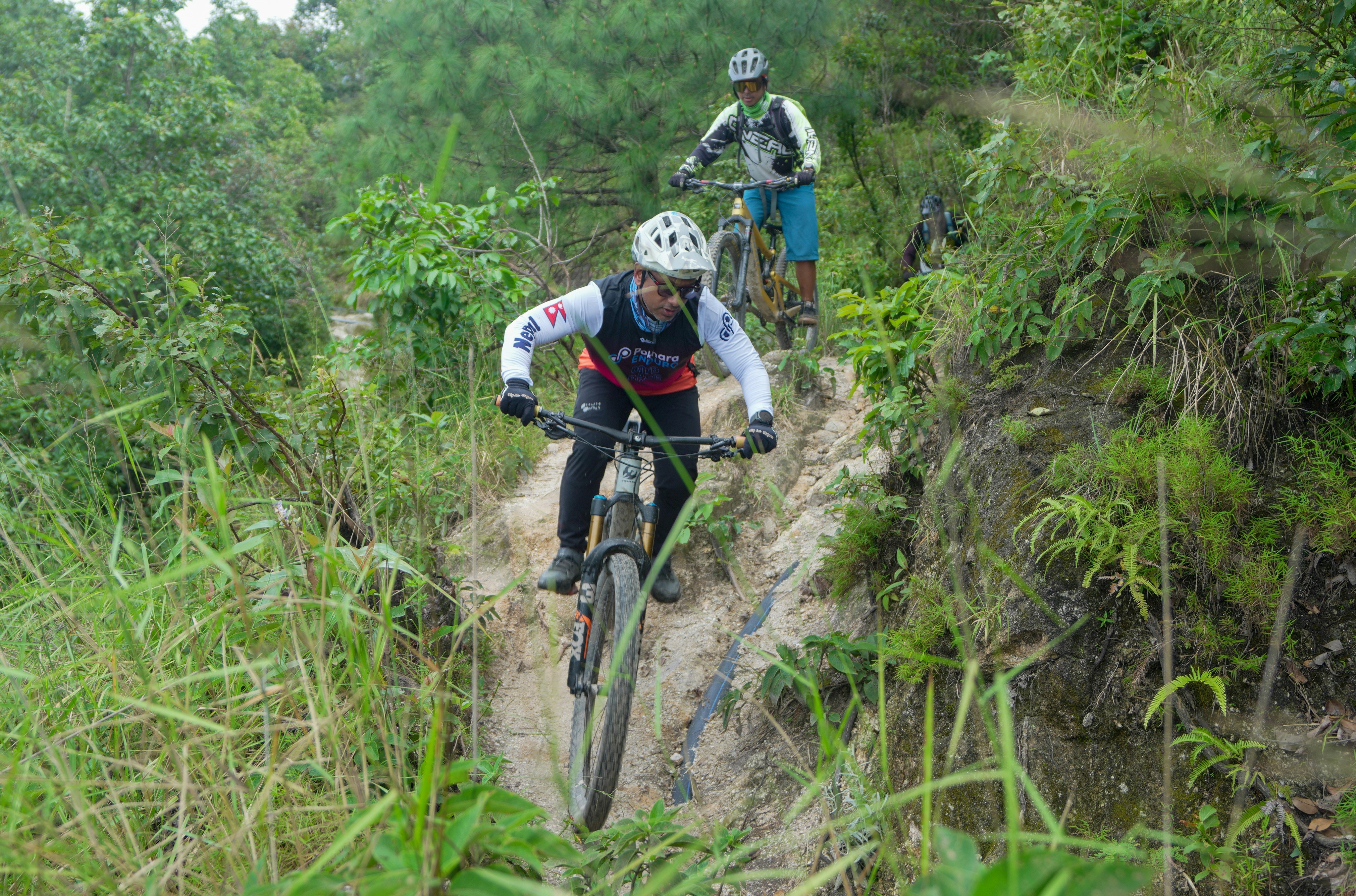 Two cyclists riding downhill on a dirt path.