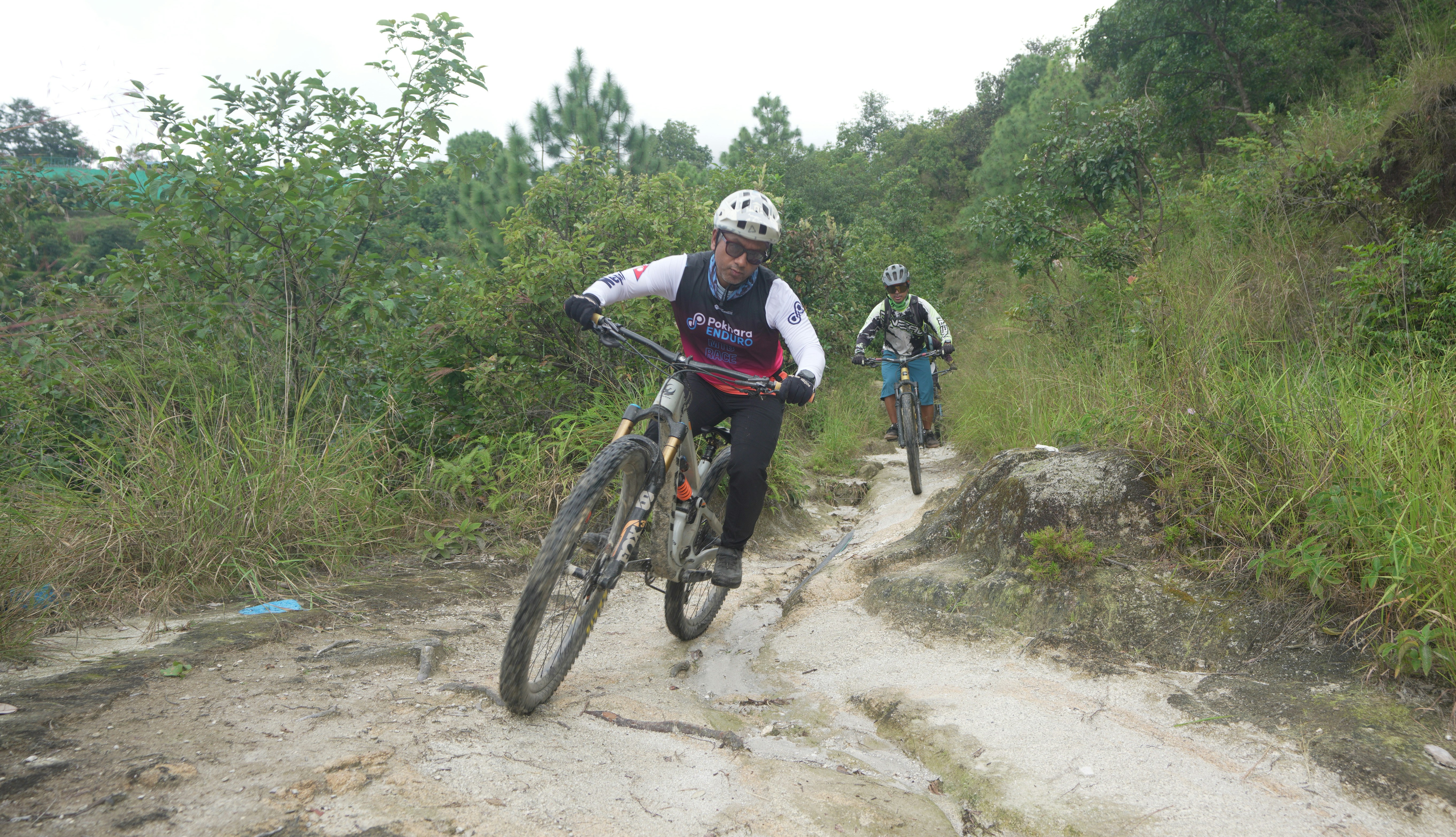 Two cyclists ride mountain bikes on a dirt path.