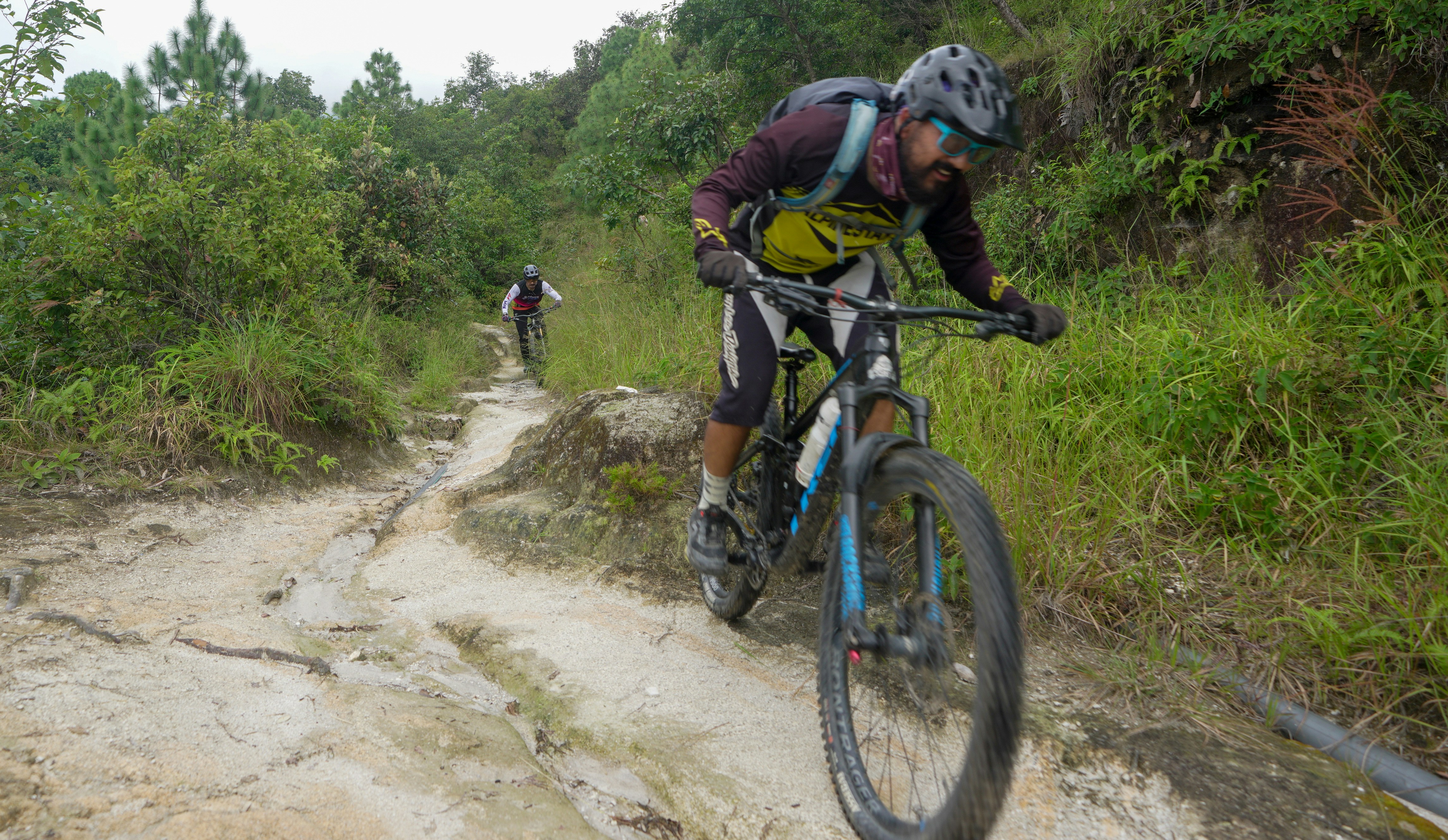 Two cyclists riding on a muddy mountain trail.