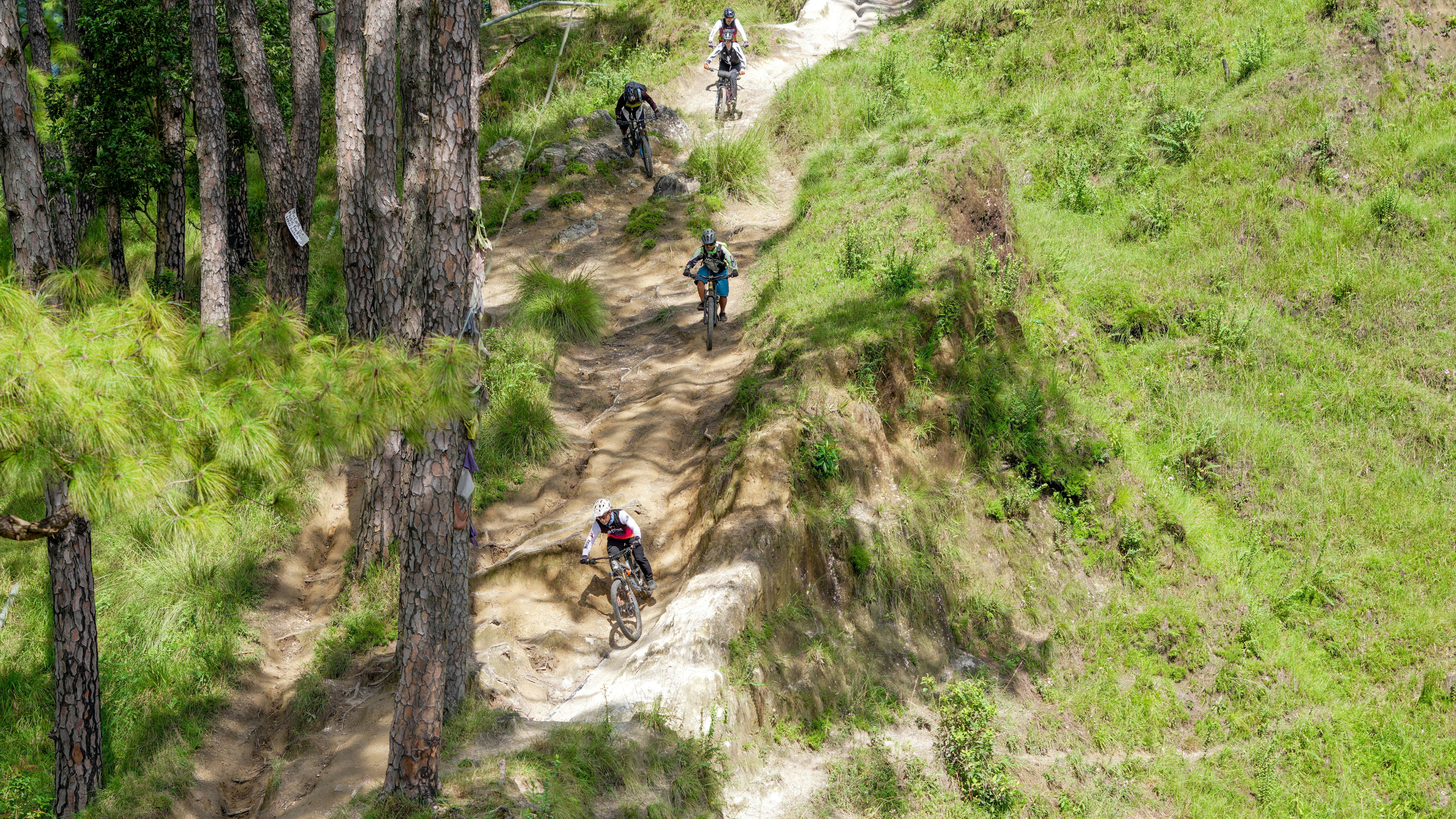 People biking down a steep, winding dirt path.
