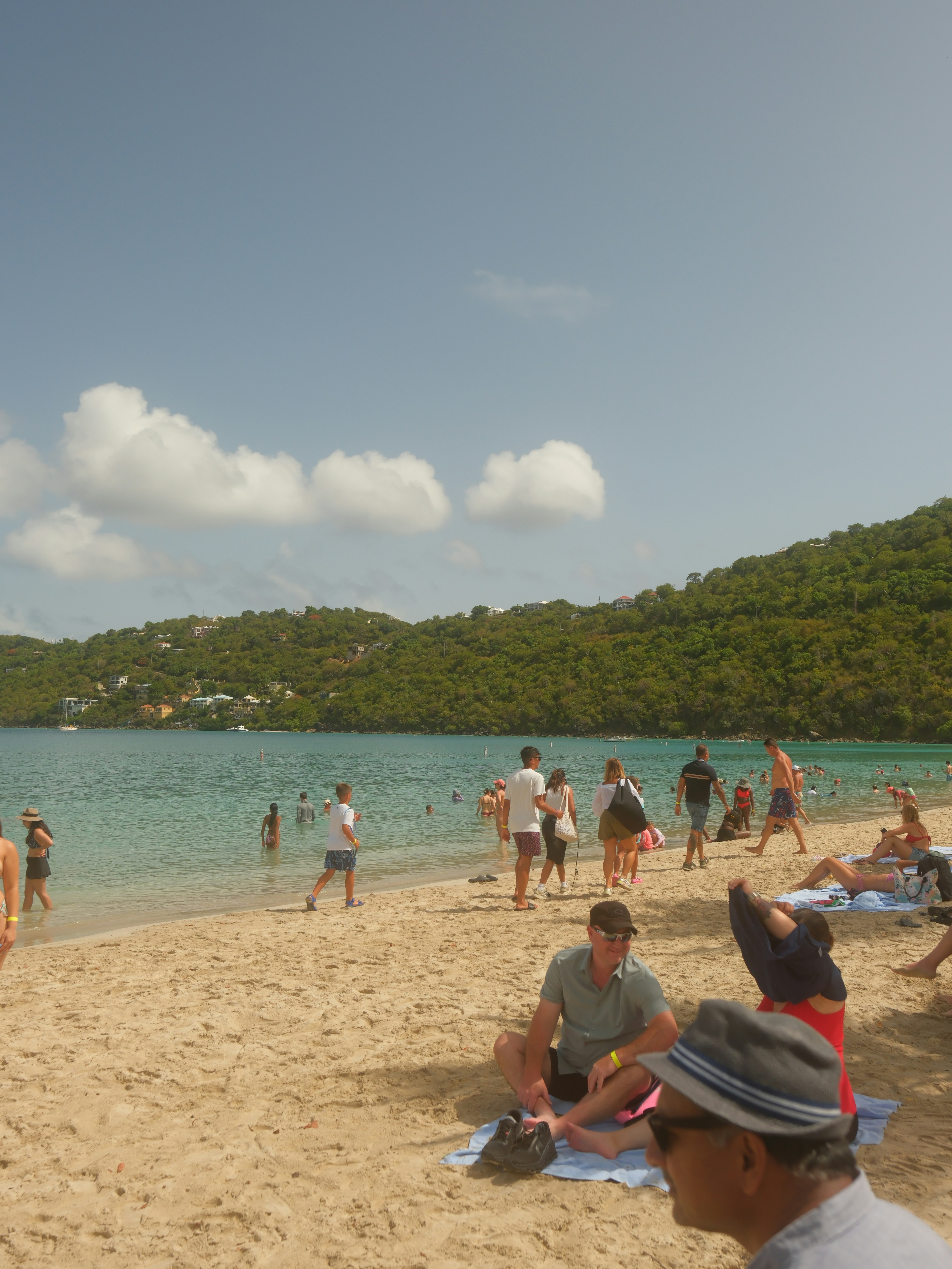People relaxing on a sunny beach with green hills.