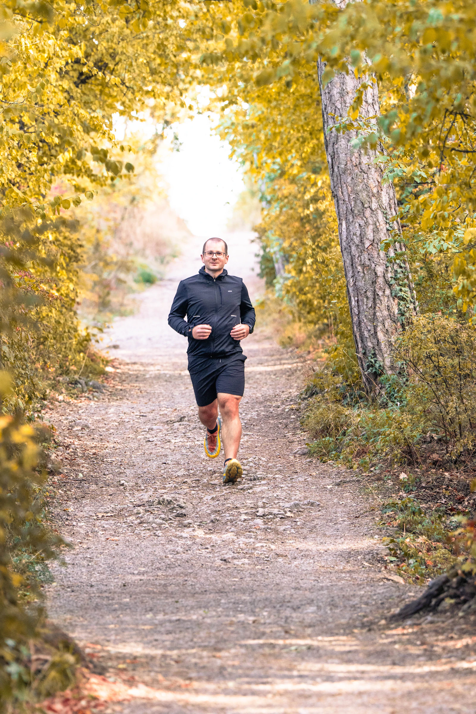 Man running on a forest trail through autumn leaves.