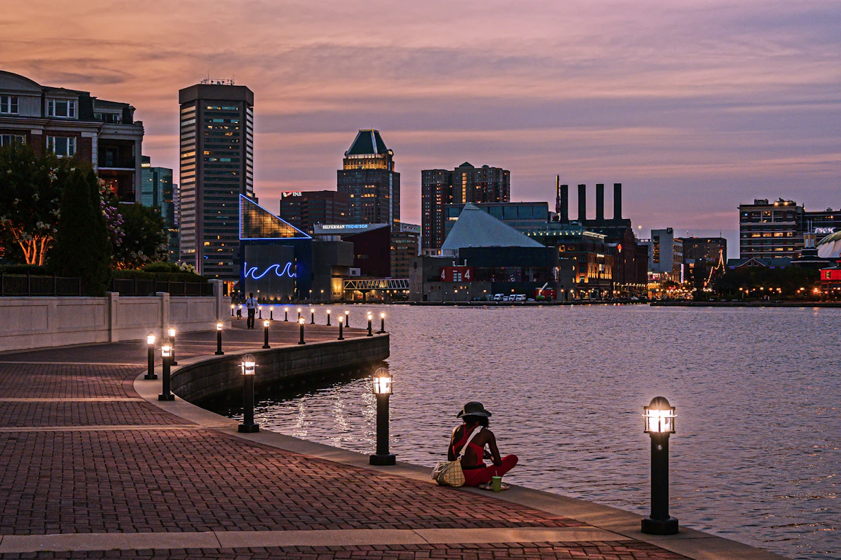 Person sitting by waterfront overlooking city skyline at dusk.