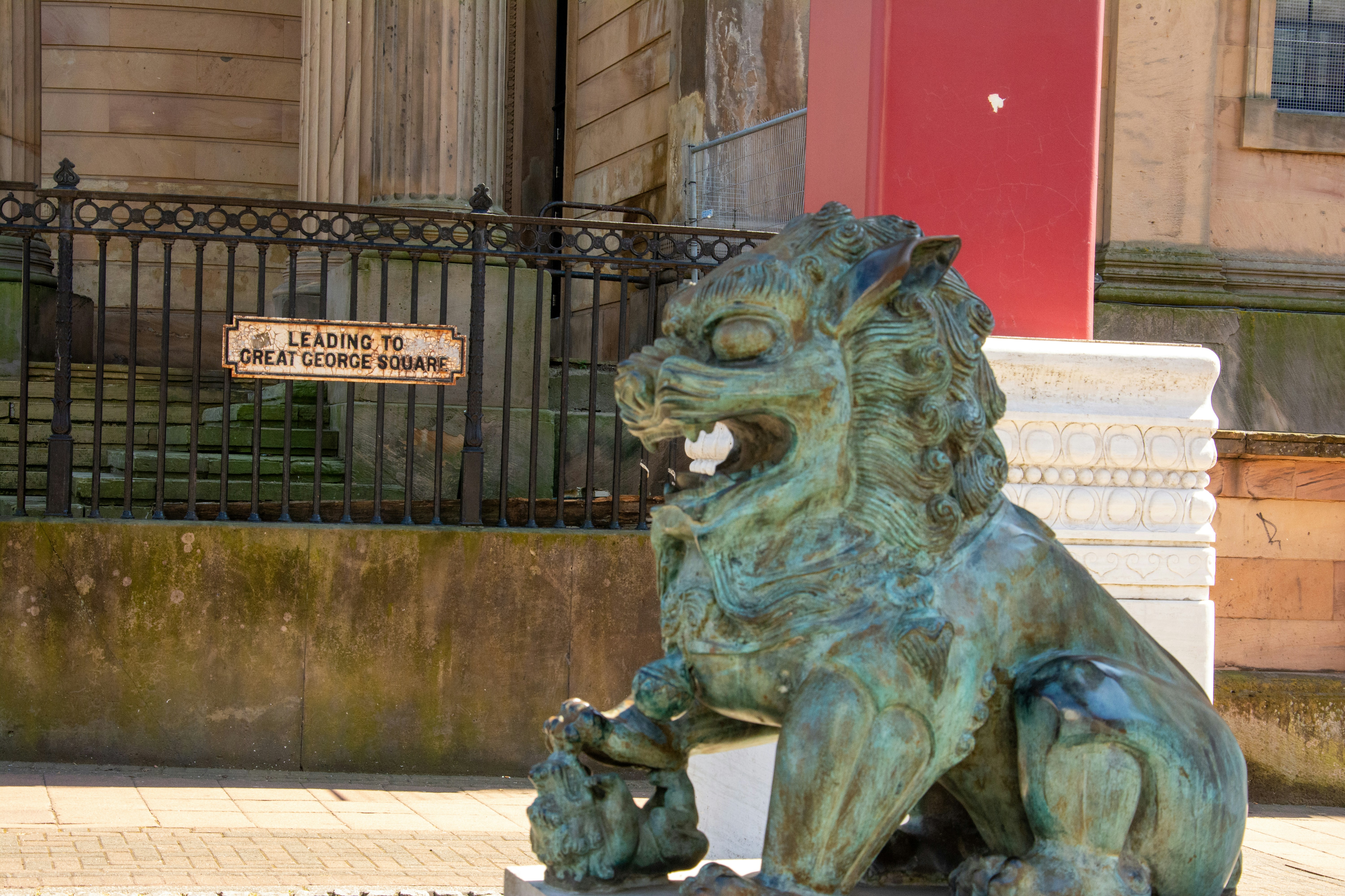 A weathered bronze lion statue guards a building entrance. photo – Free ...