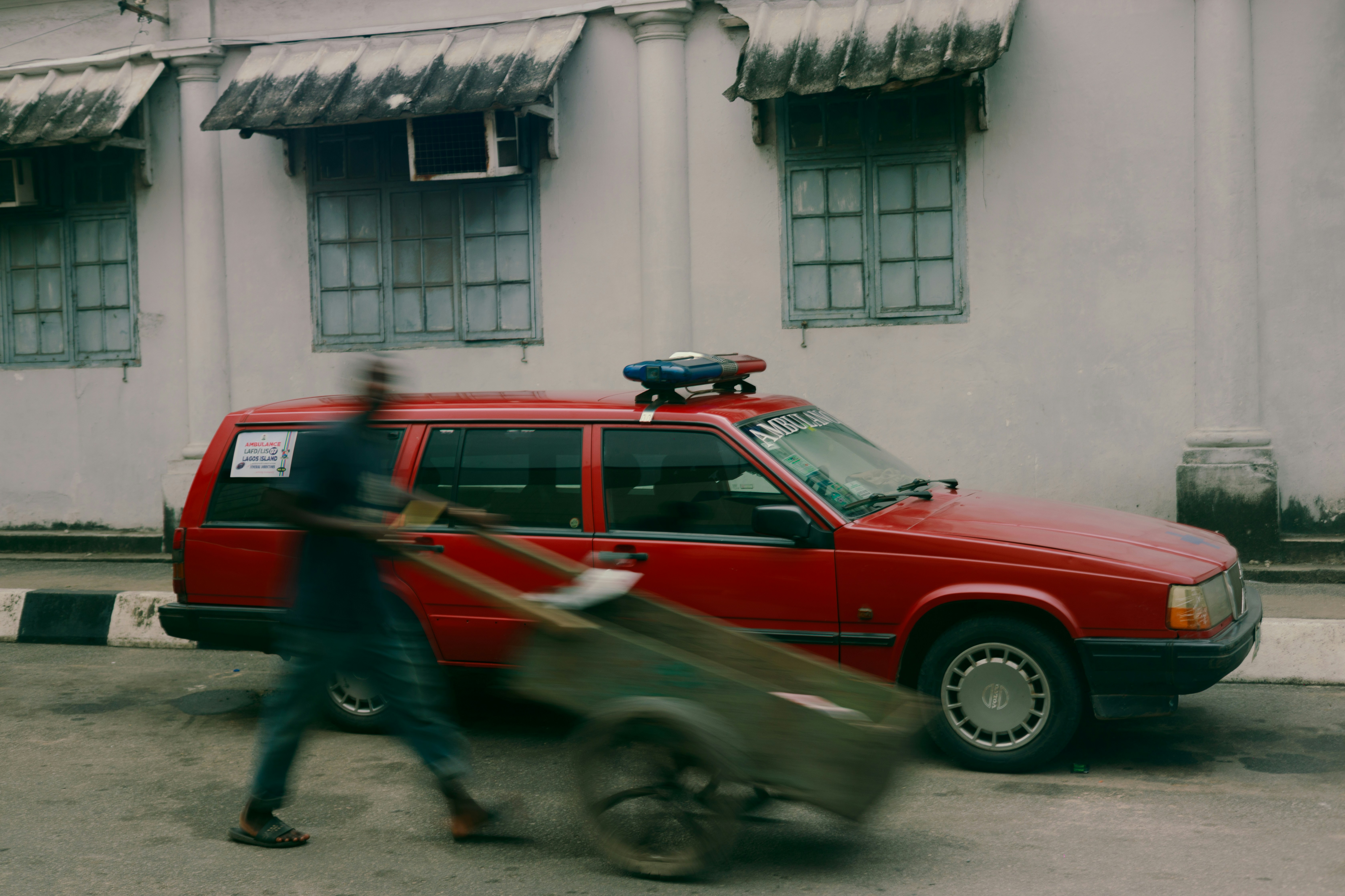 Man pushes cart past red car on street.