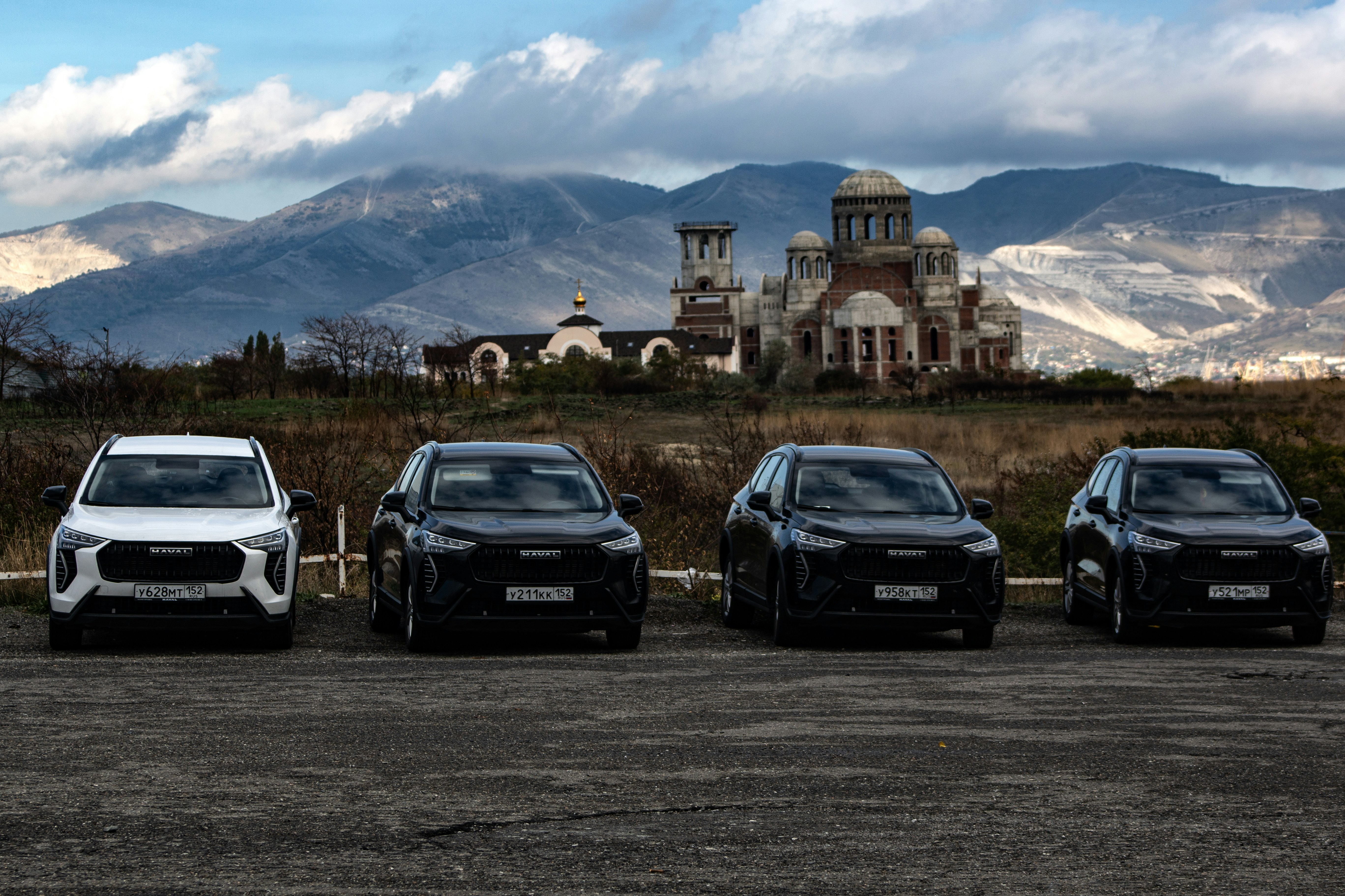 electric SUV comparison road - Four cars parked with a building and mountains behind.