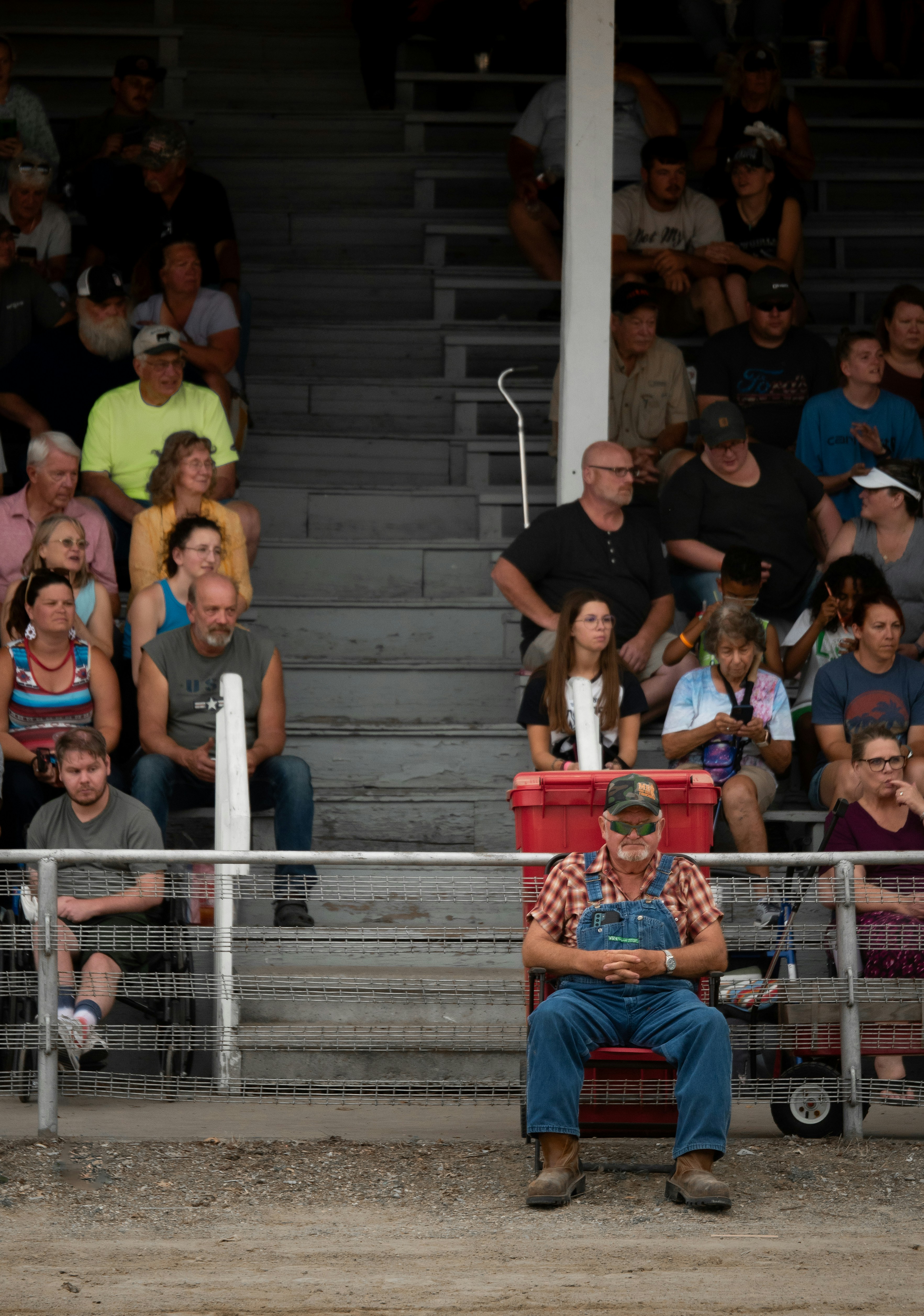 Man in overalls sits alone in stadium seating.