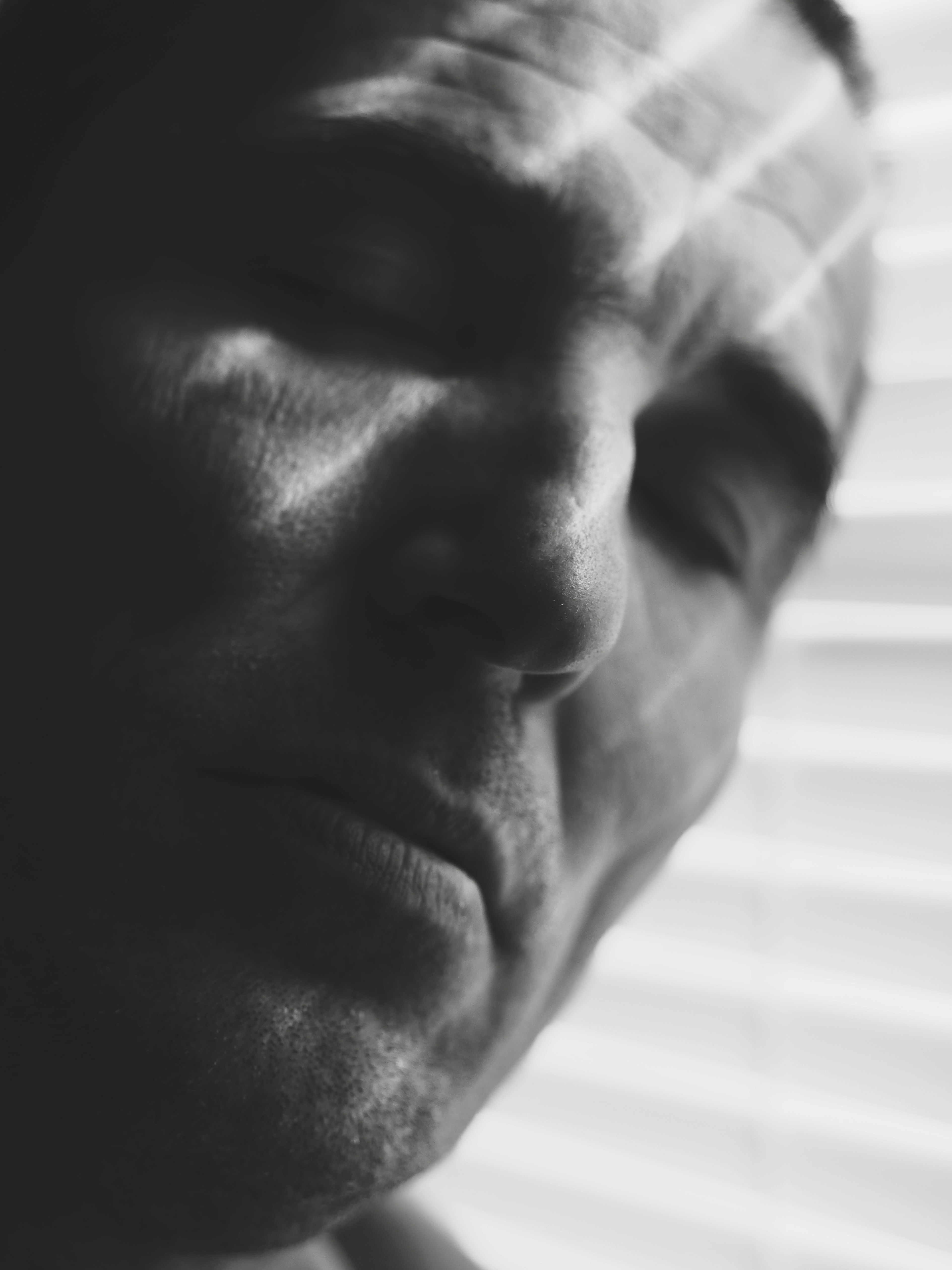 Close-up of a man's face with blinds casting shadows.