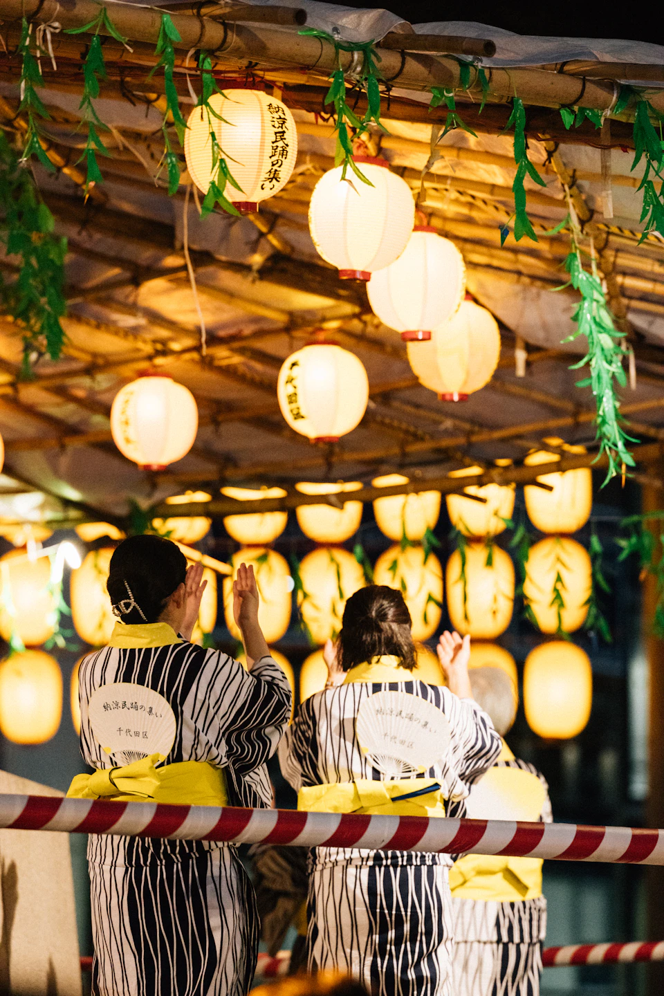 People in yukata walking past glowing paper lanterns at a Japanese summer festival at night