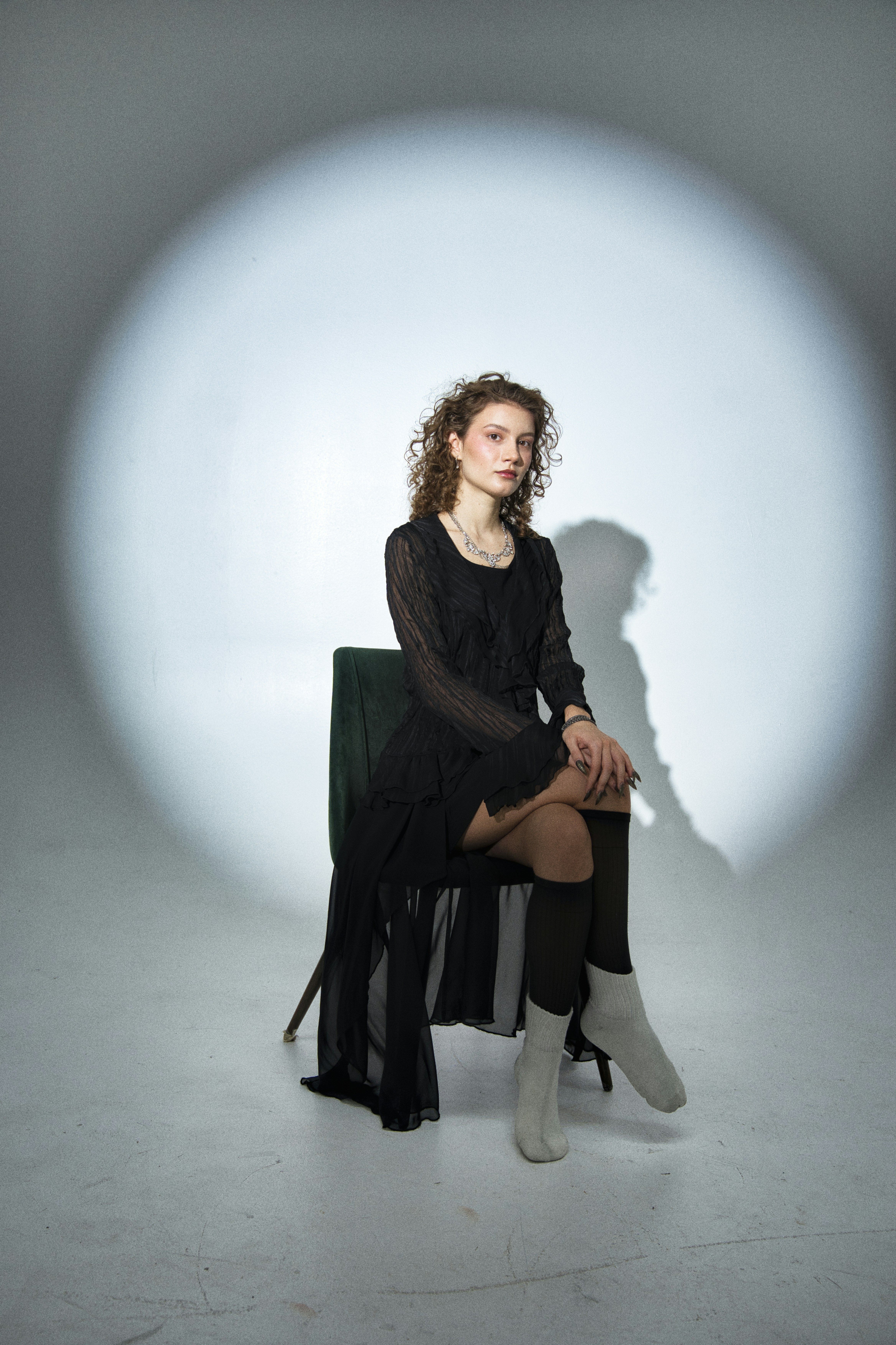 Woman in black dress sitting on chair under spotlight.