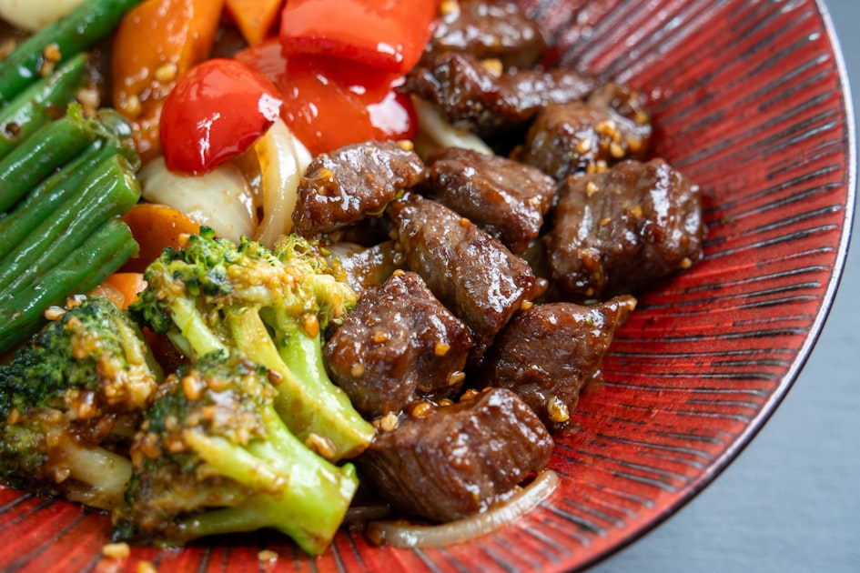 Cubed beef stir-fried with vegetables on a red plate — the visual signature of bò lúc lắc.