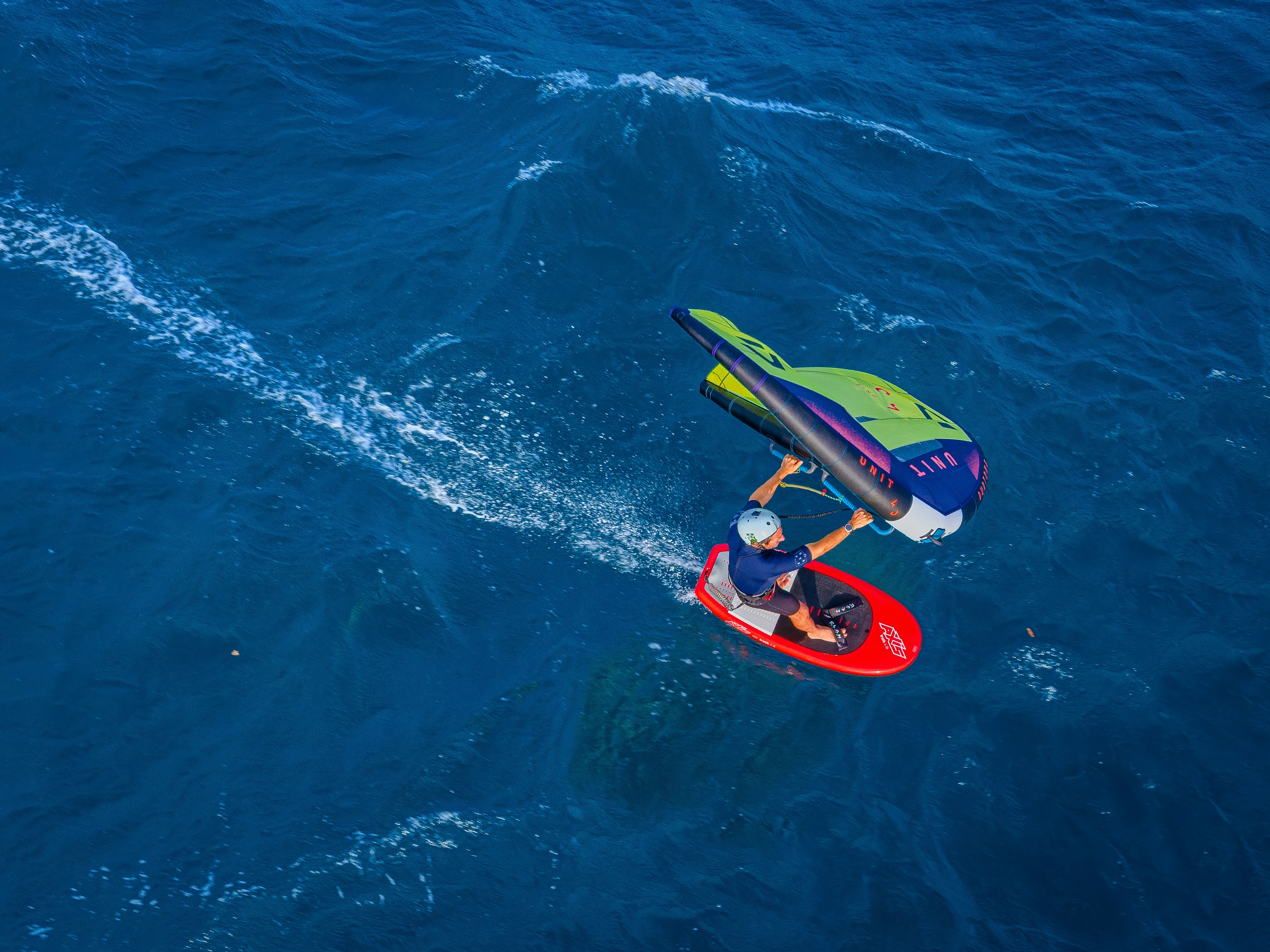 Person wing foiling on a red board in the ocean.