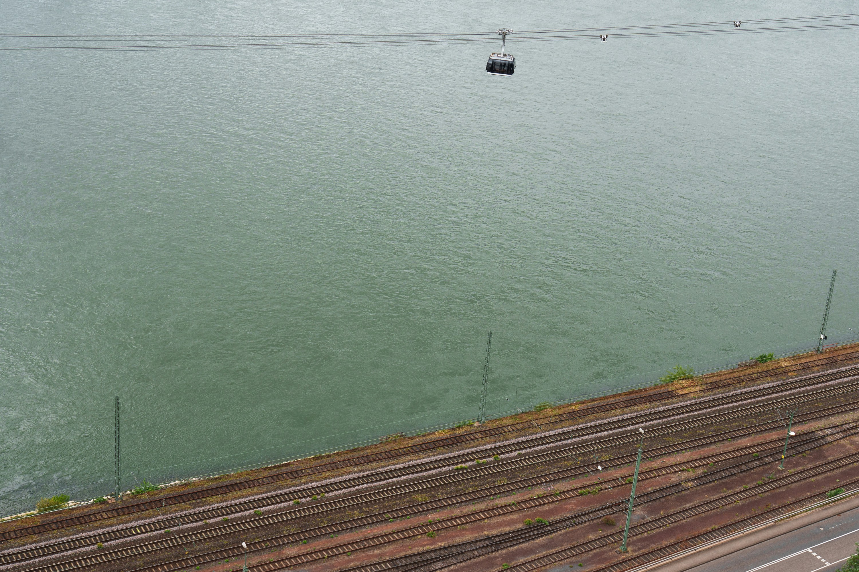 Cable car over a river next to train tracks.