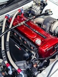 Close-up of a shiny red car engine with metal hoses.