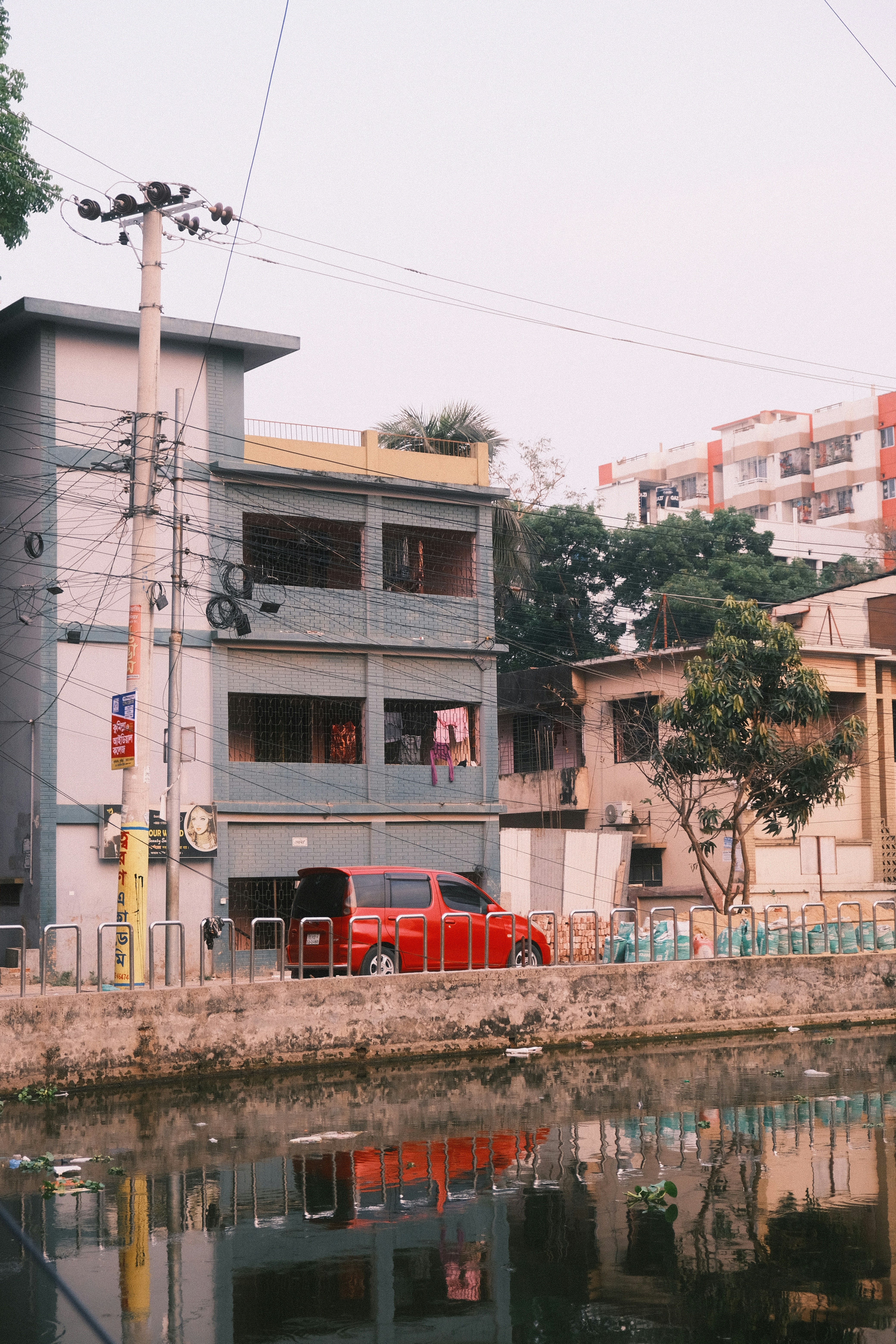 Red car parked by a building next to water.
