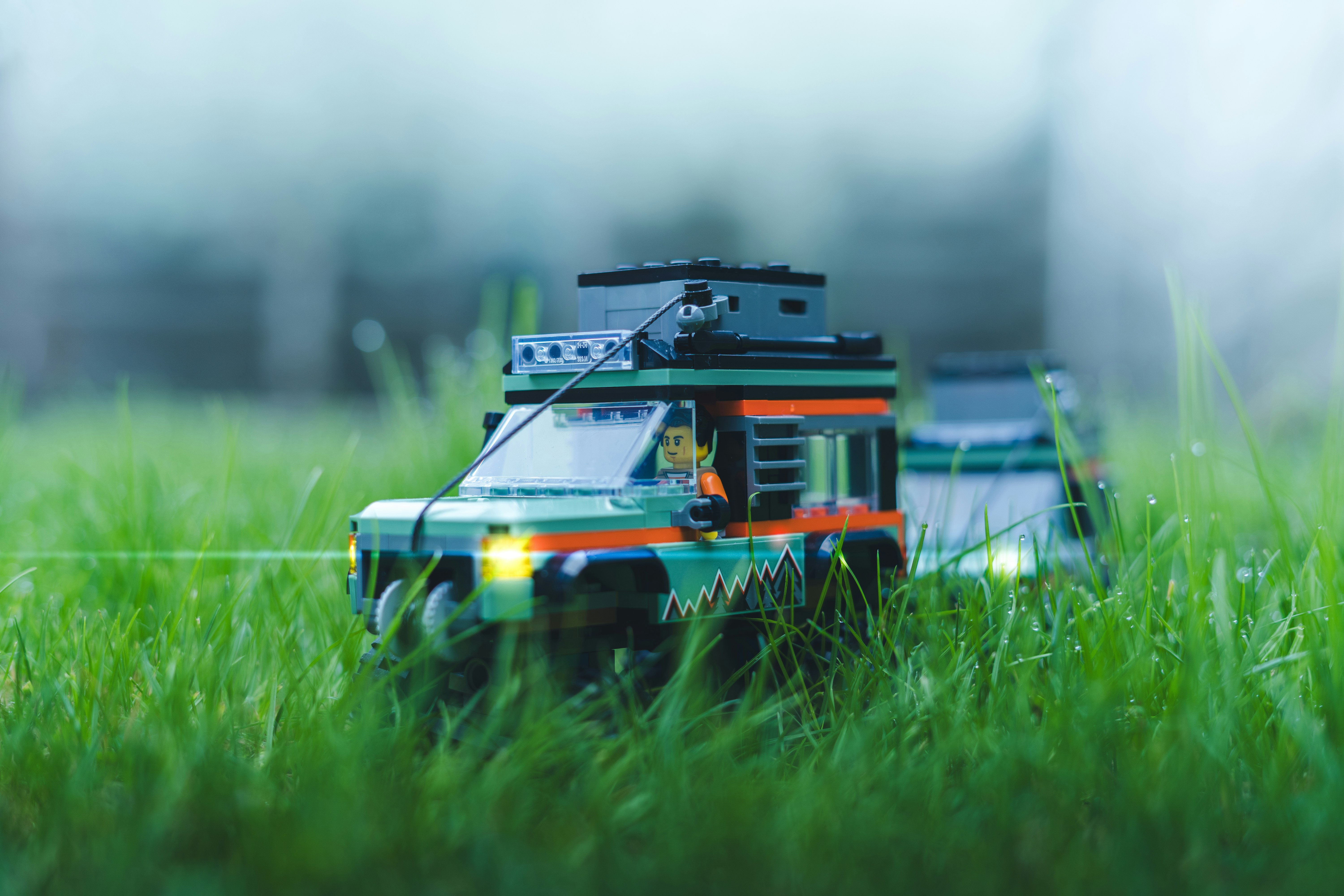 Two green toy cars with trailers in grass