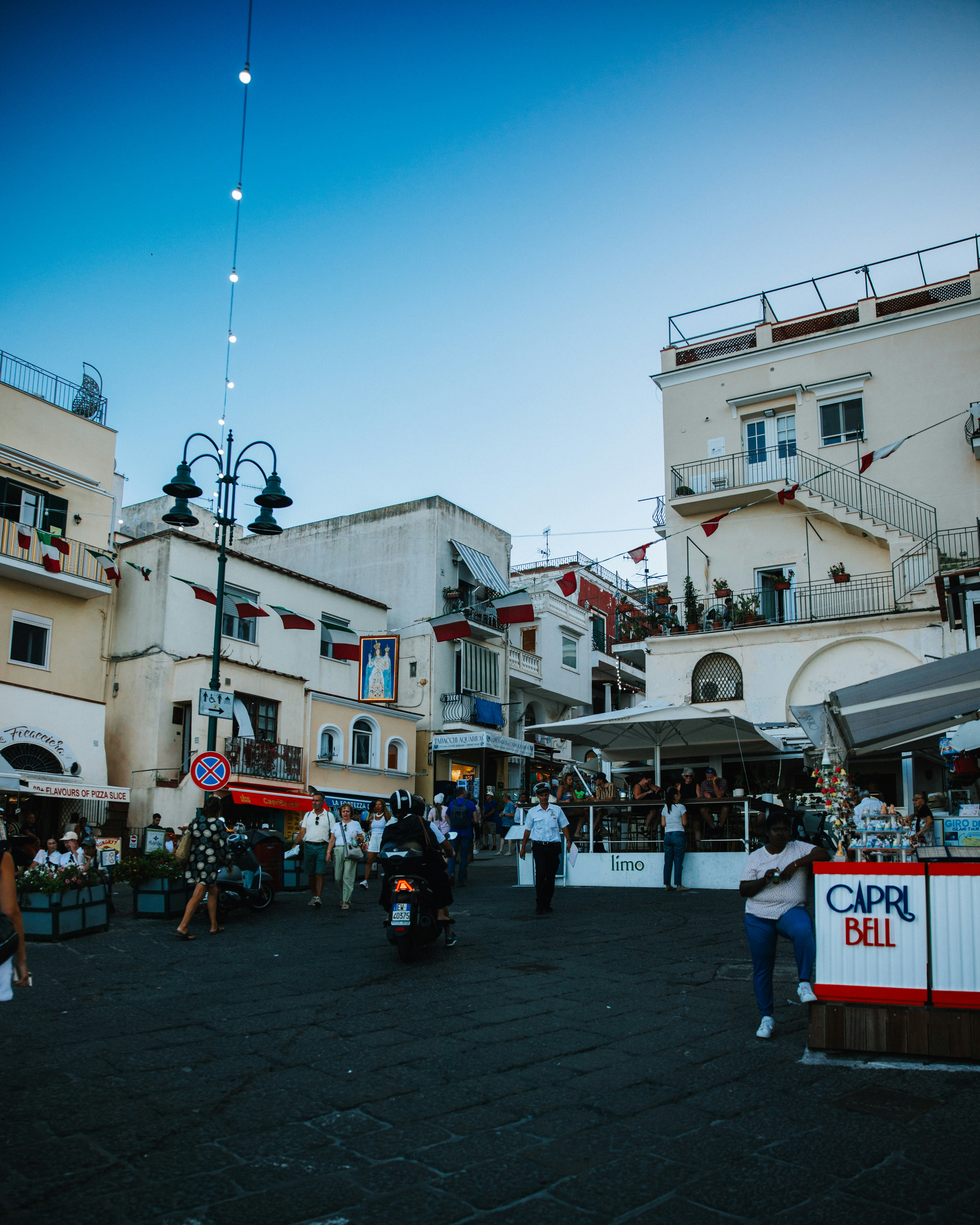 Pedoni passeggiano lungo una strada acciottolata in un paese mediterraneo.