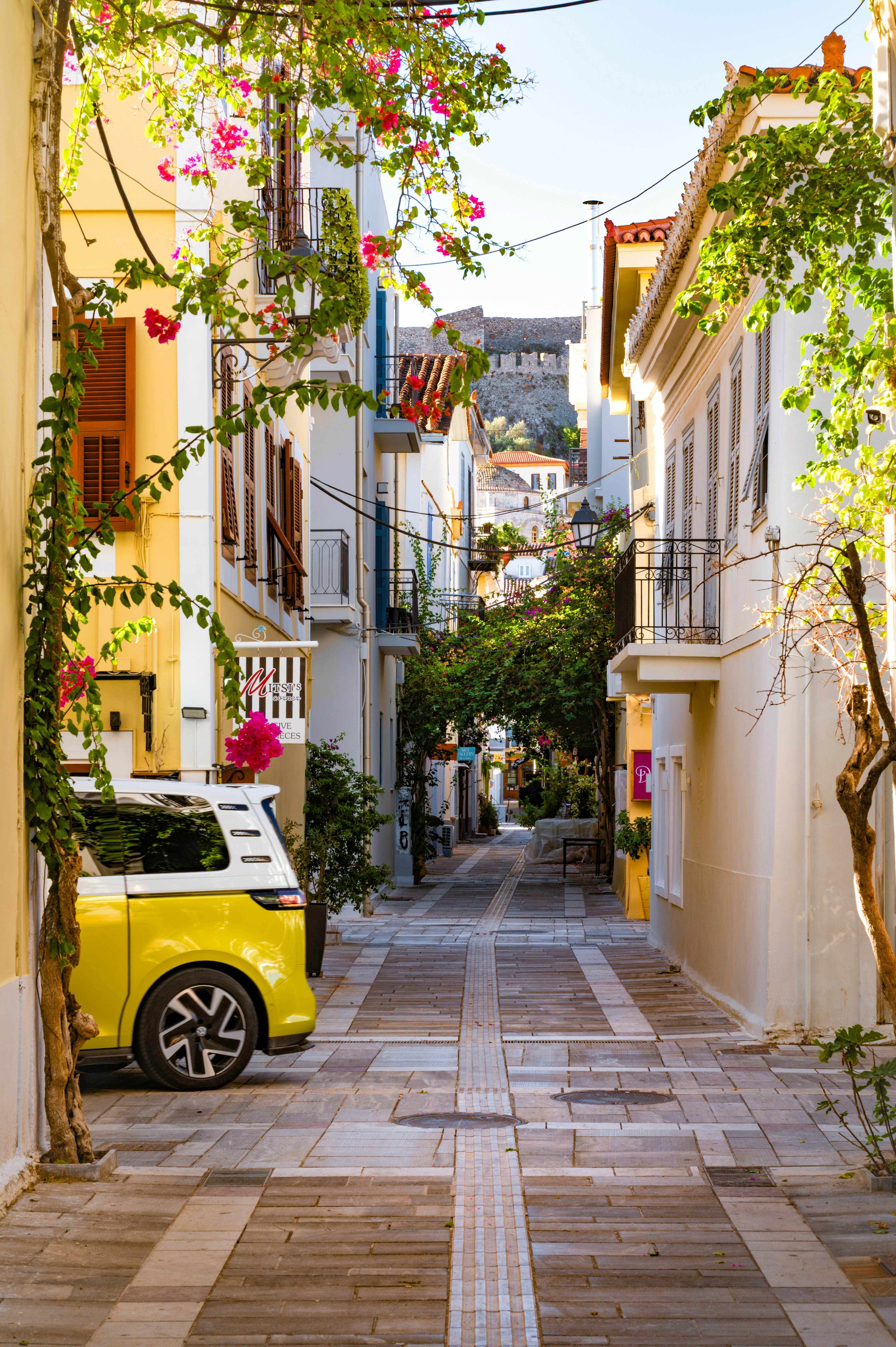 Narrow street with yellow car and blooming flowers.