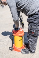 Man operating a yellow and orange pressure sprayer outdoors.