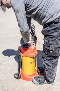 Man operating a yellow and orange pressure sprayer outdoors.