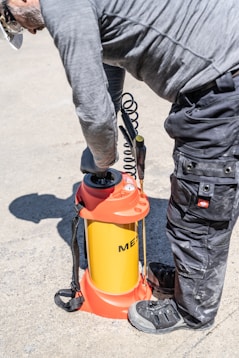 Man operating a yellow and orange pressure sprayer outdoors.