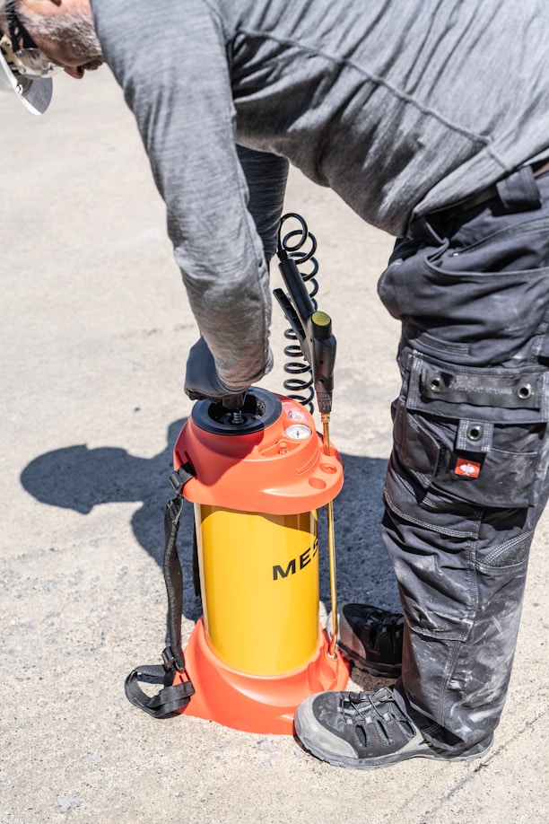 Man operating a yellow and orange pressure sprayer outdoors.