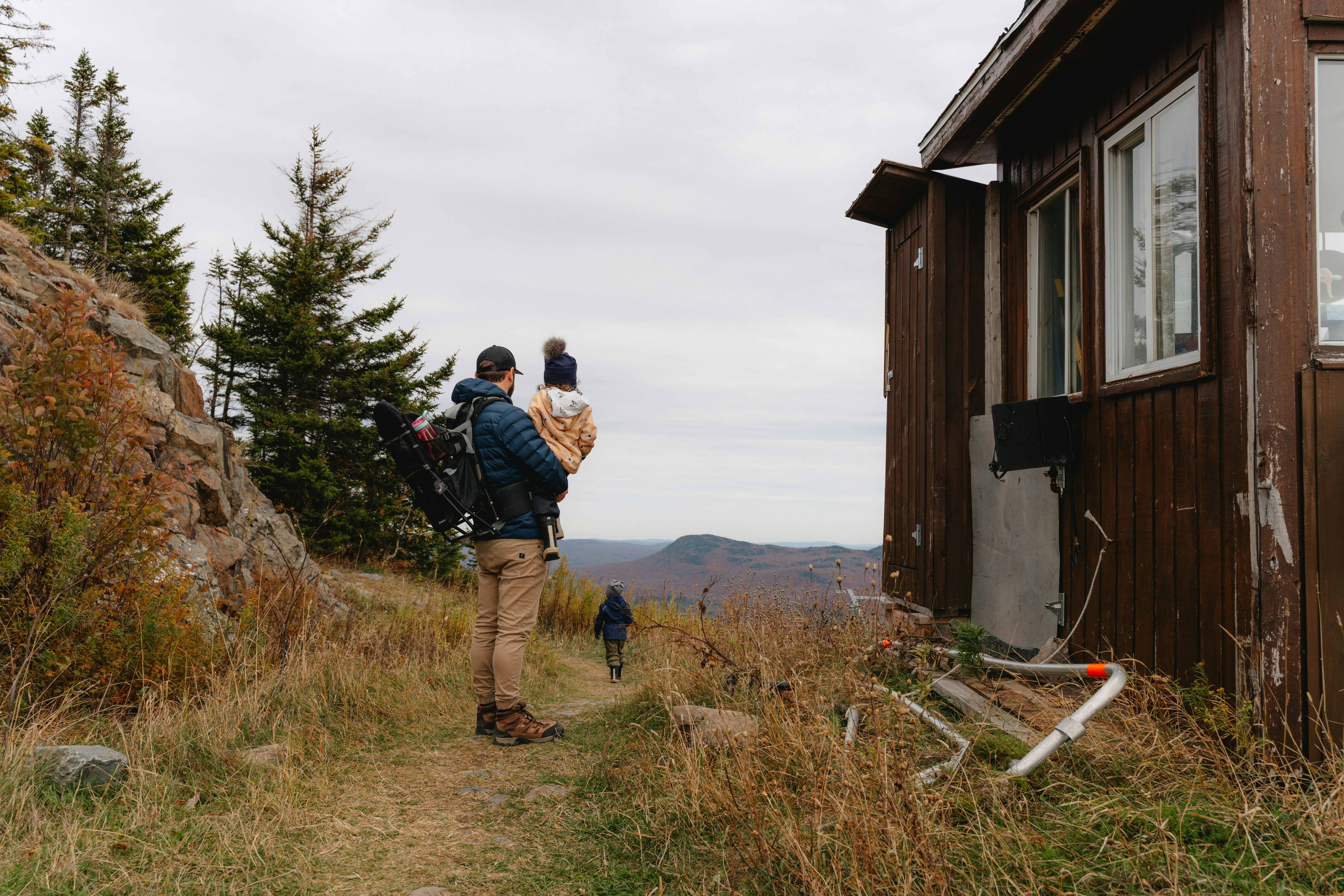 Man carrying child near rustic cabin on mountain