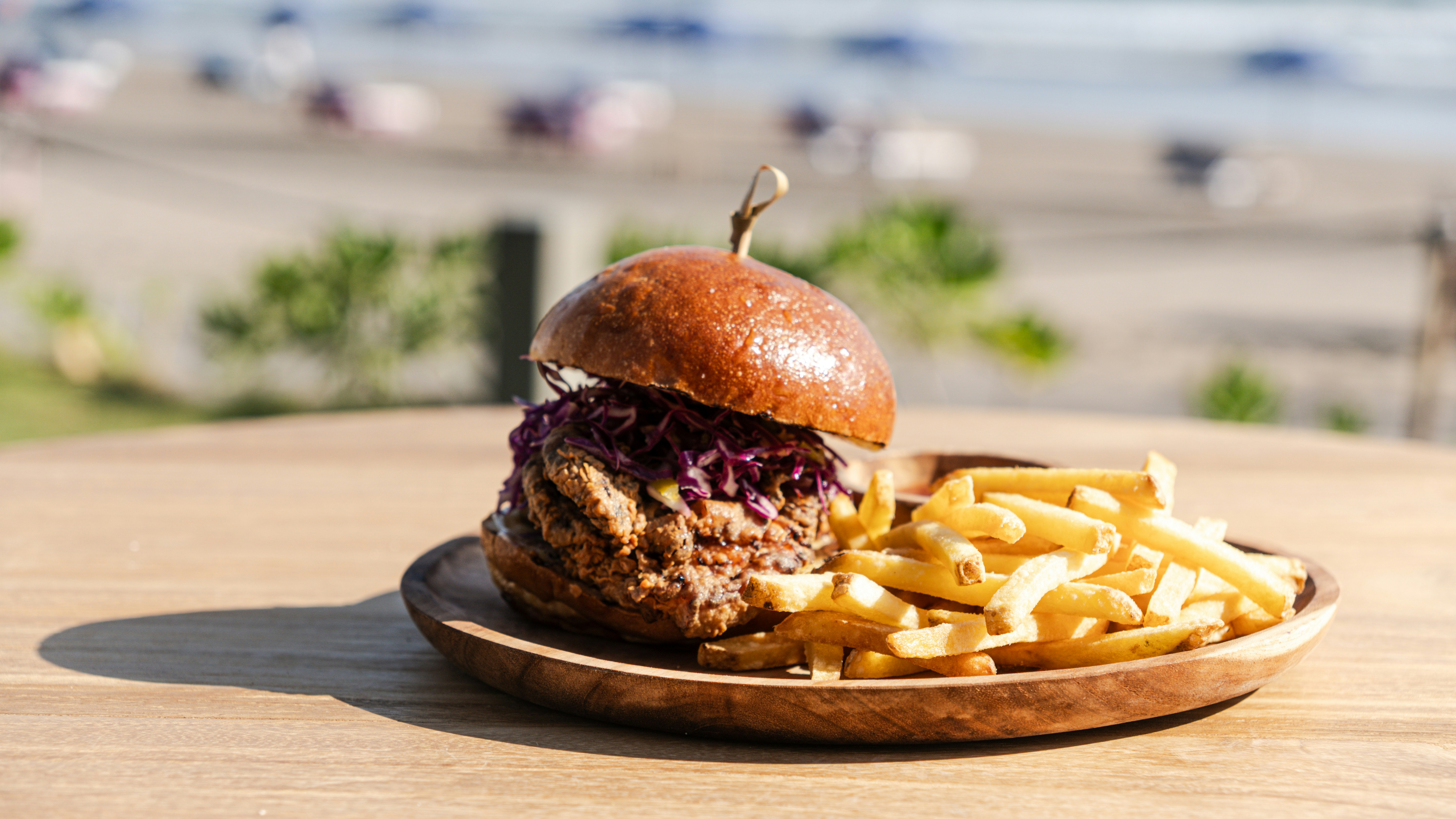 A juicy burger with fries on a wooden plate.