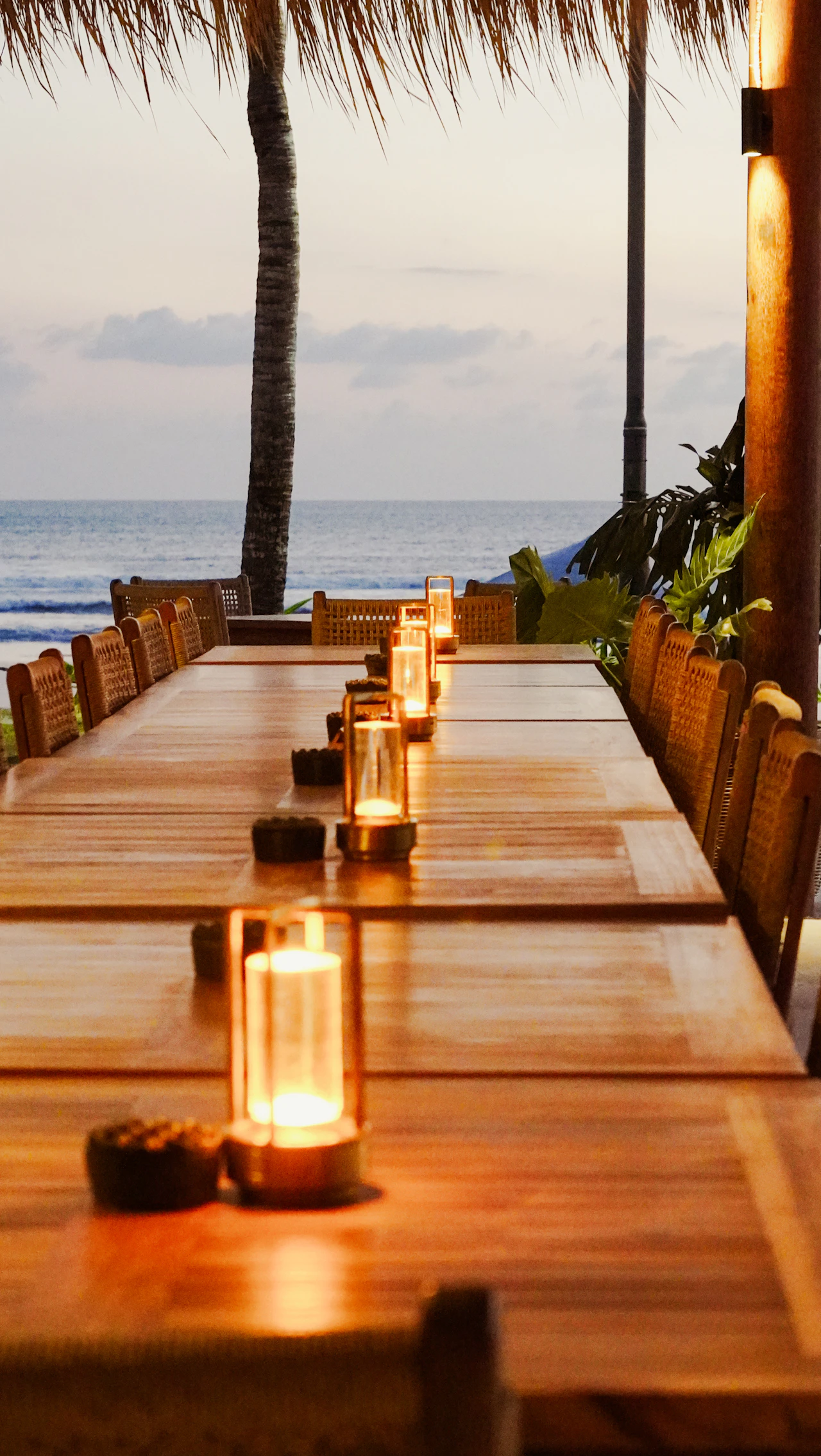 A long candle-lit wooden dining table set at the edge of a view