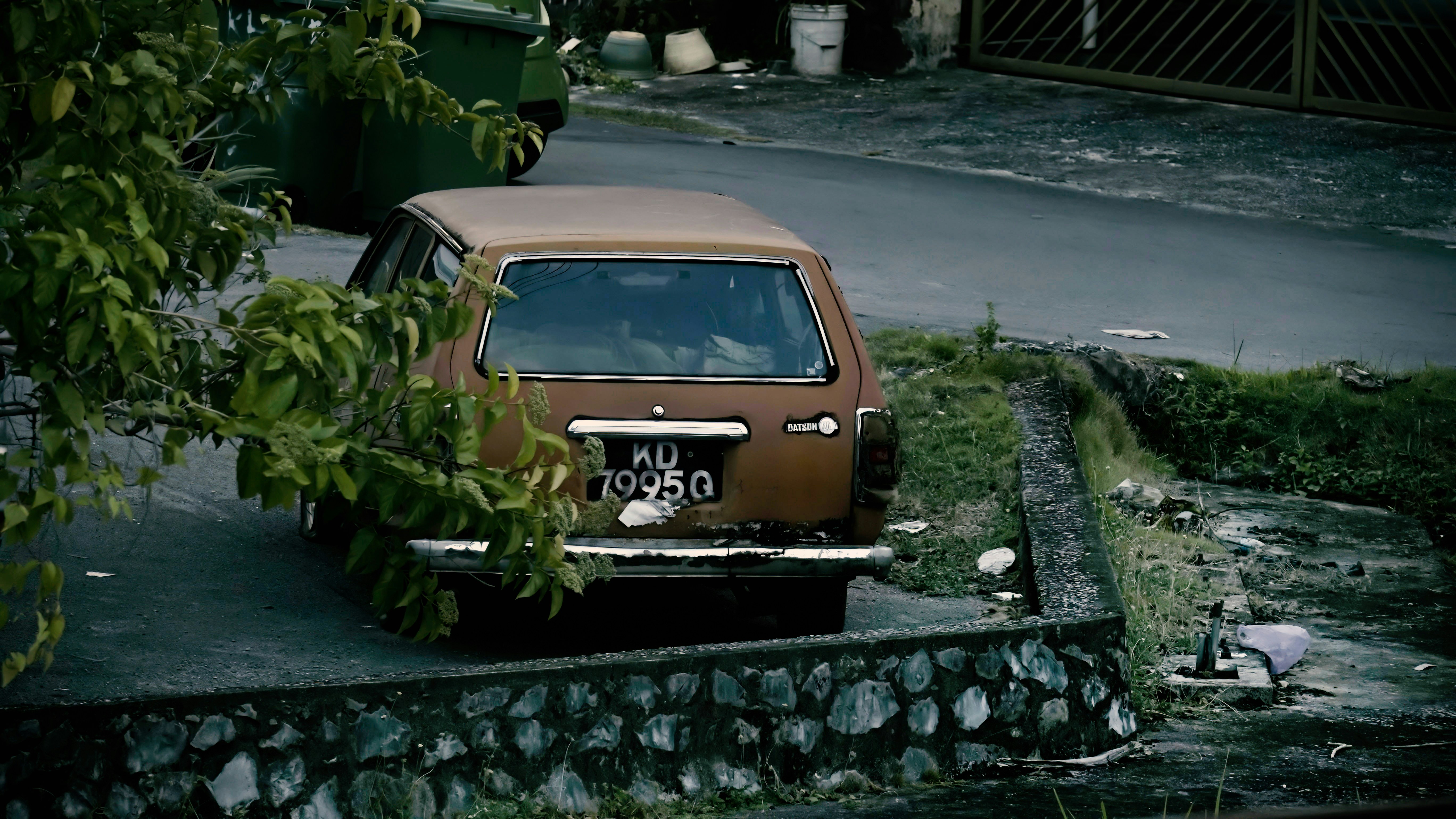 Un auto marrón oxidado estacionado junto a una calle.