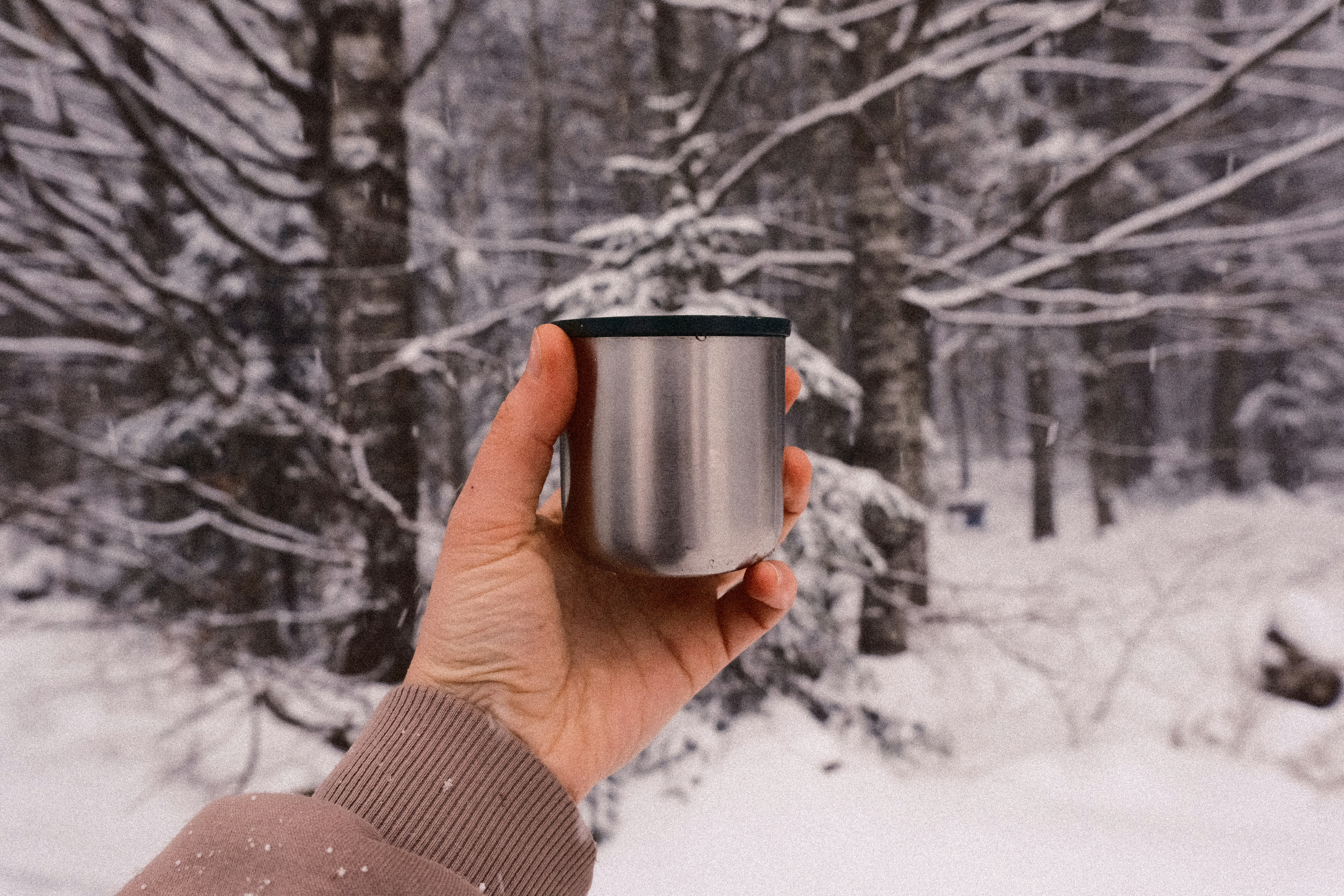 Hand holding metal mug in snowy forest