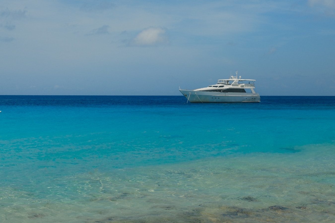 A white yacht floats on clear turquoise ocean water.