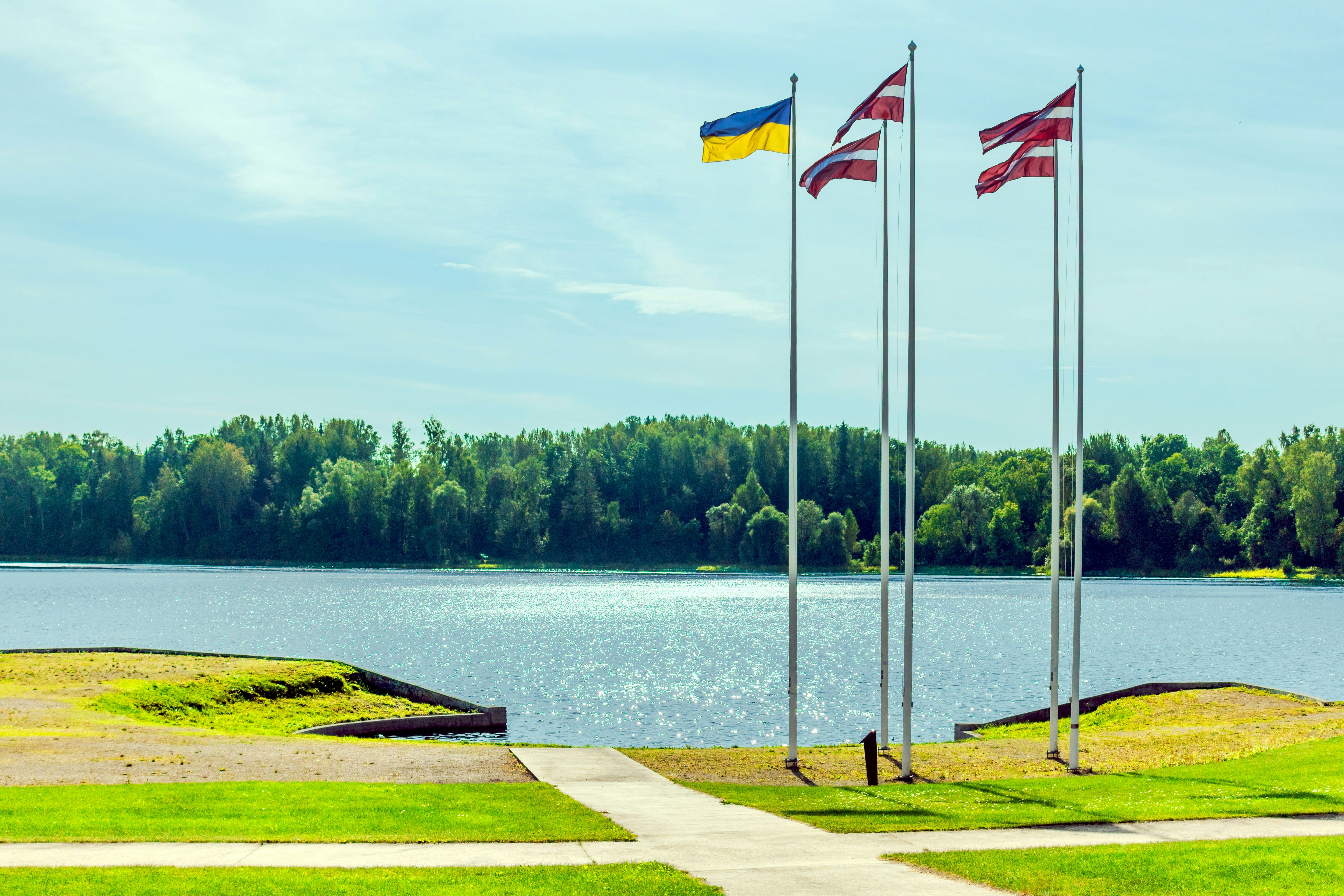 Three flags fly near a tranquil lake and forest.
