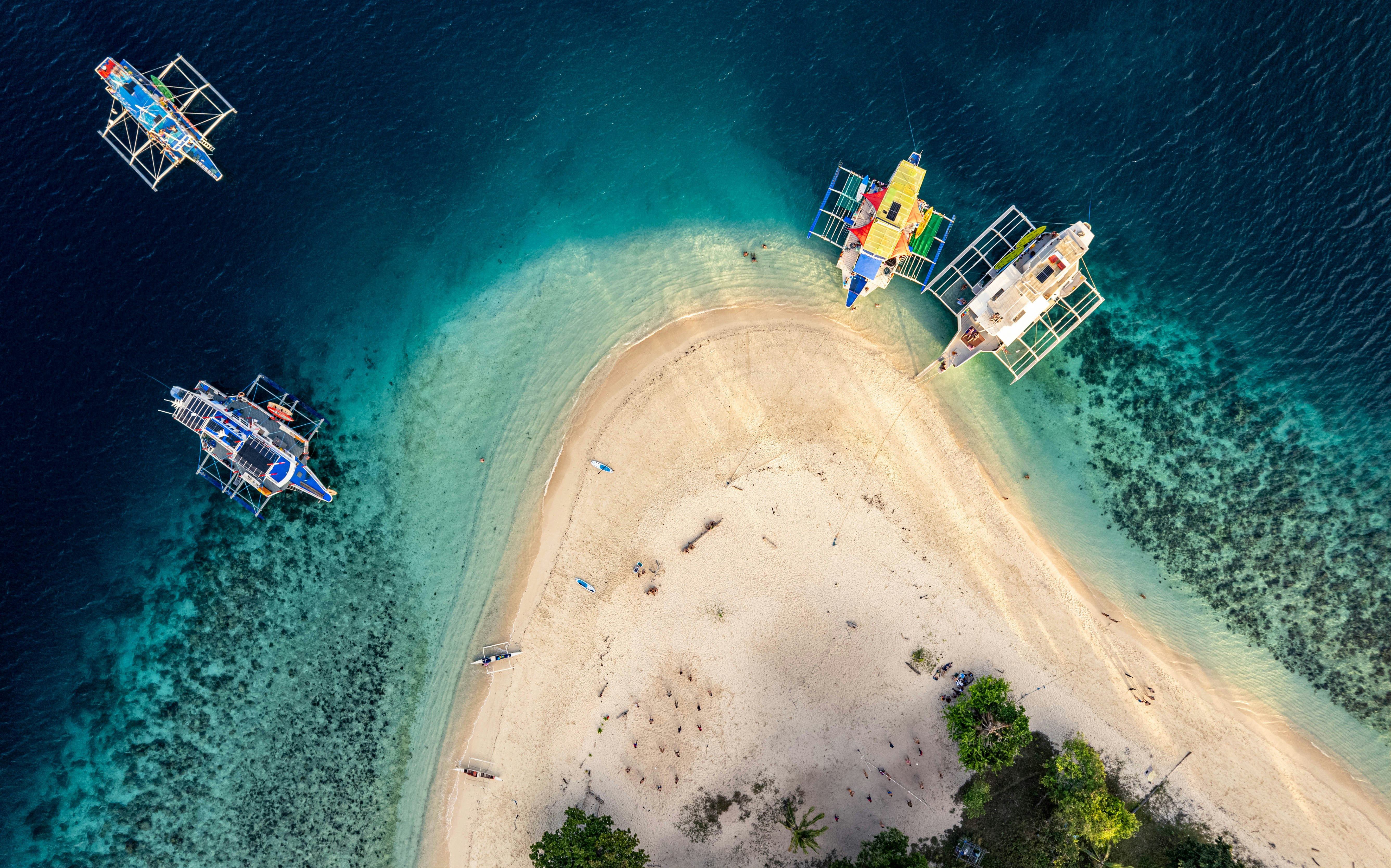 Boats anchored near a sandy island in clear blue water.