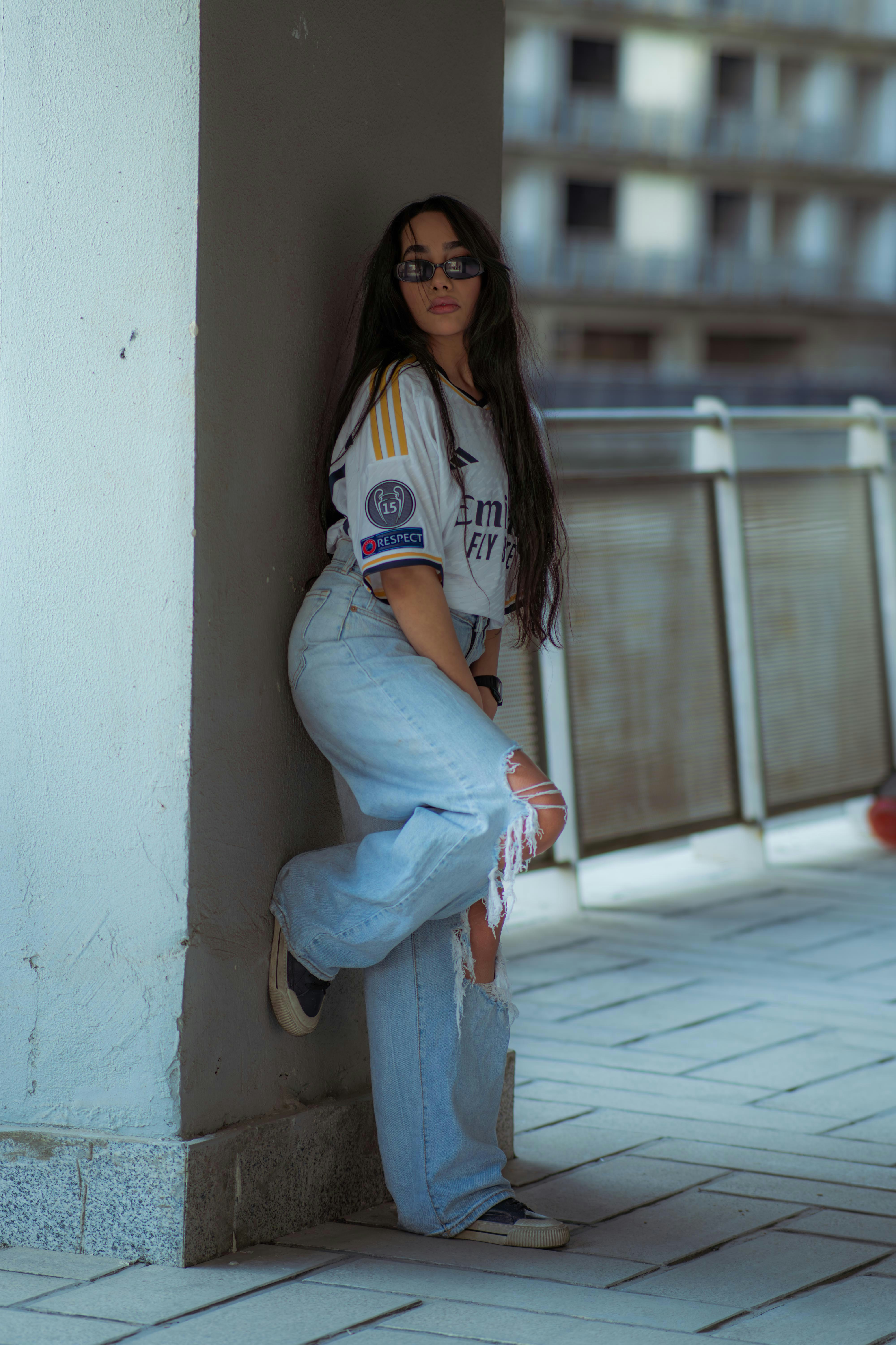 Woman in jersey and ripped jeans leaning against wall