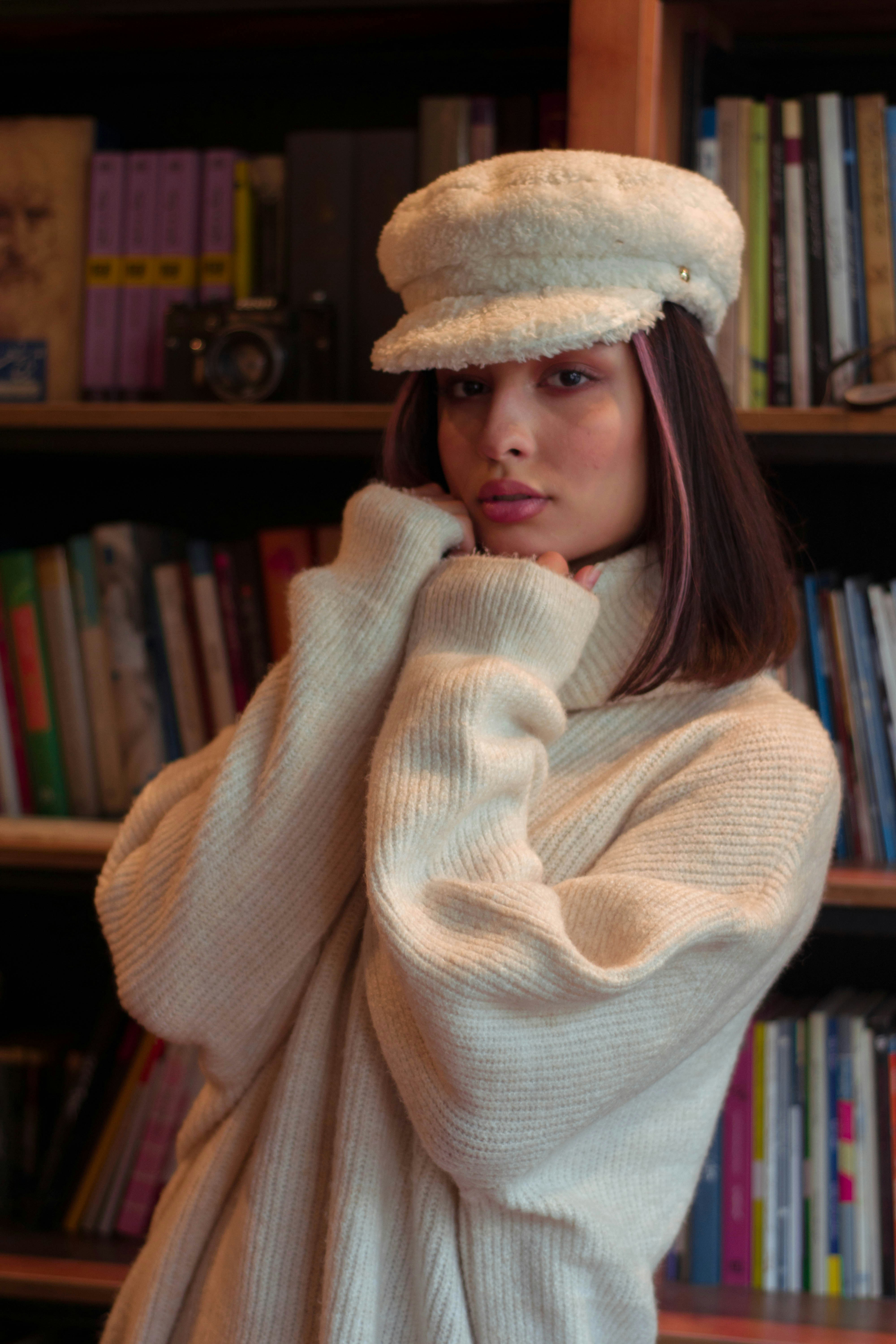 Woman wearing a cream sweater and hat indoors.