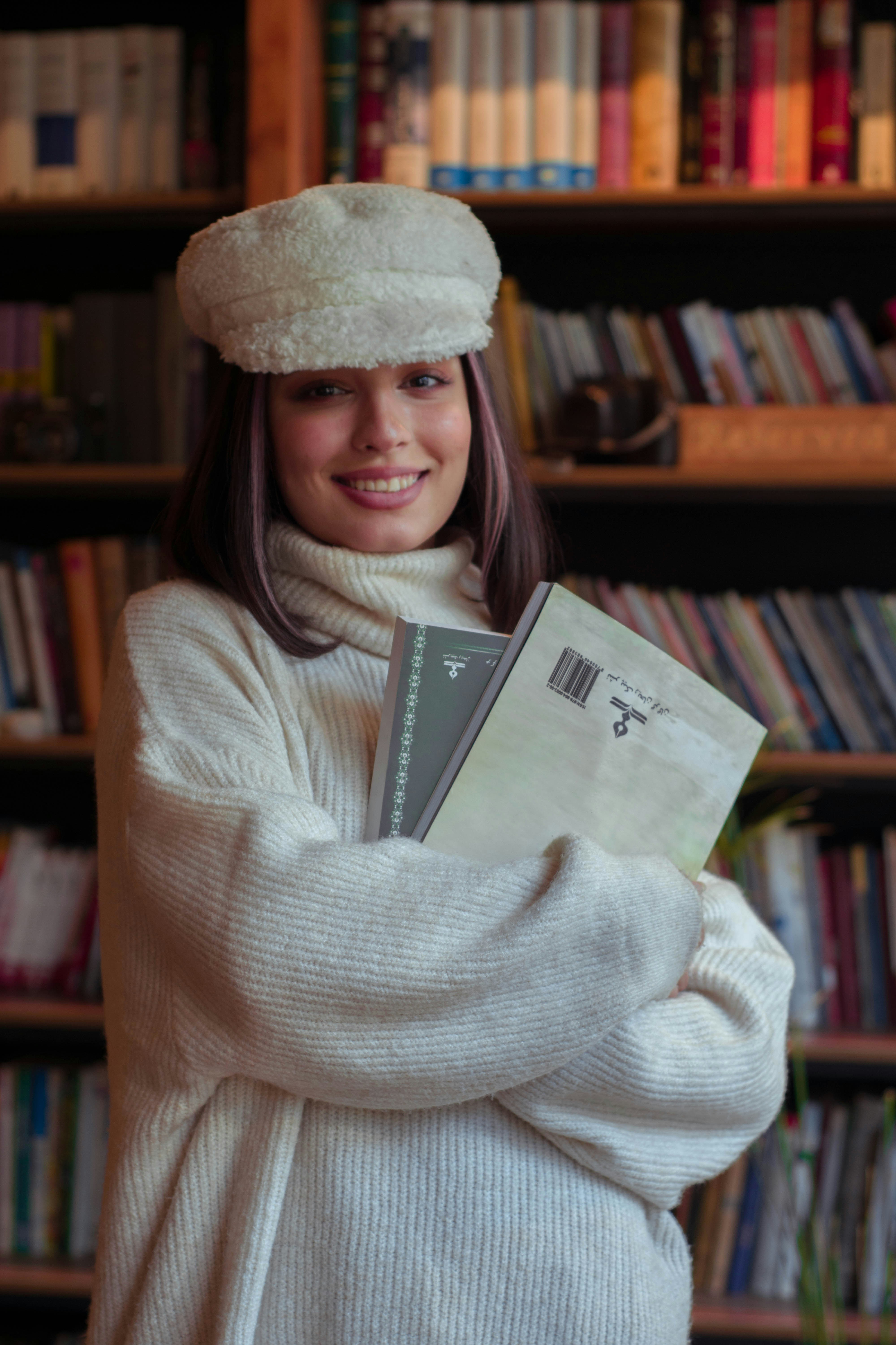 図書館で本を持っている居心地の良いセーターを着た若い女性
