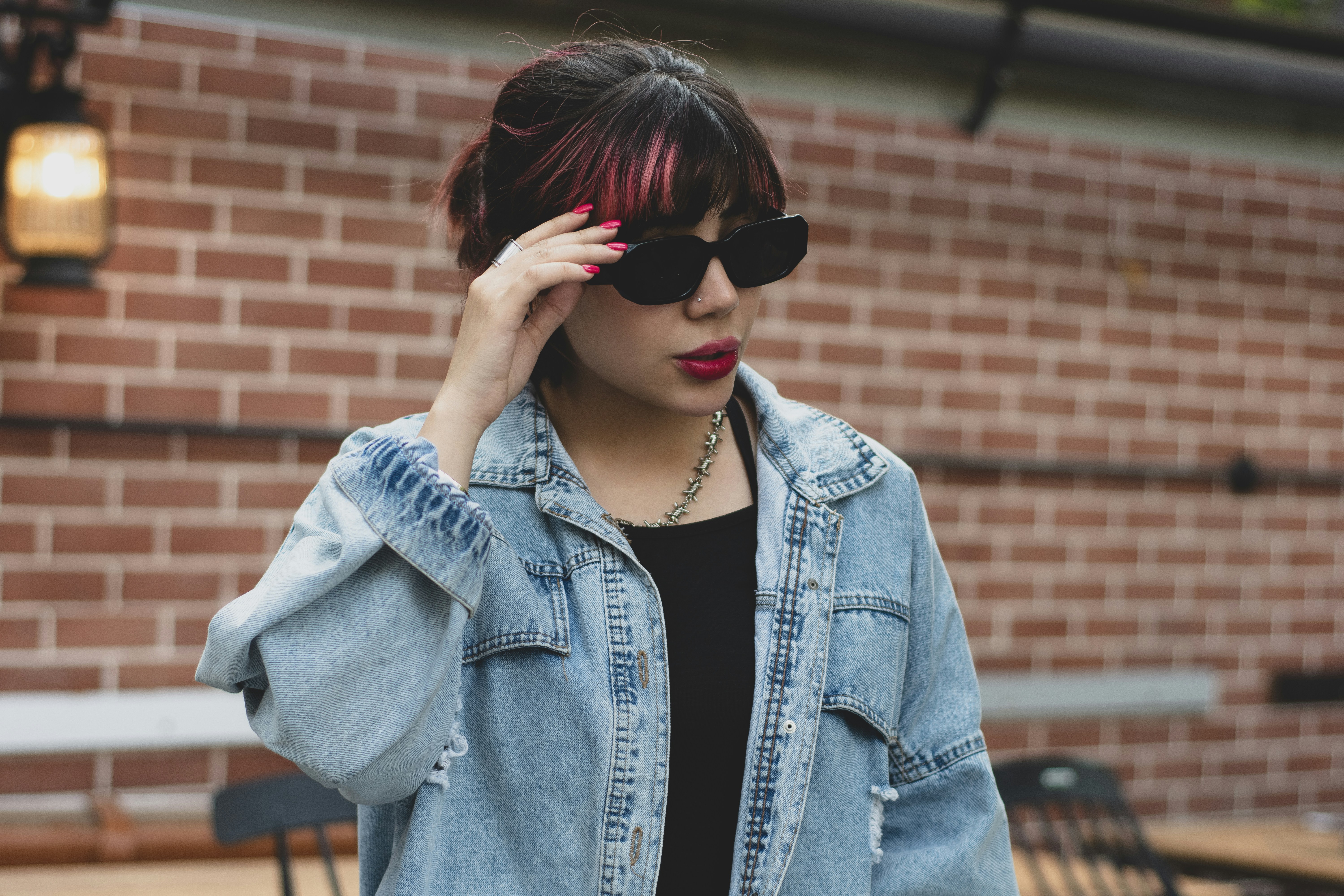 Woman in denim jacket adjusts sunglasses outdoors