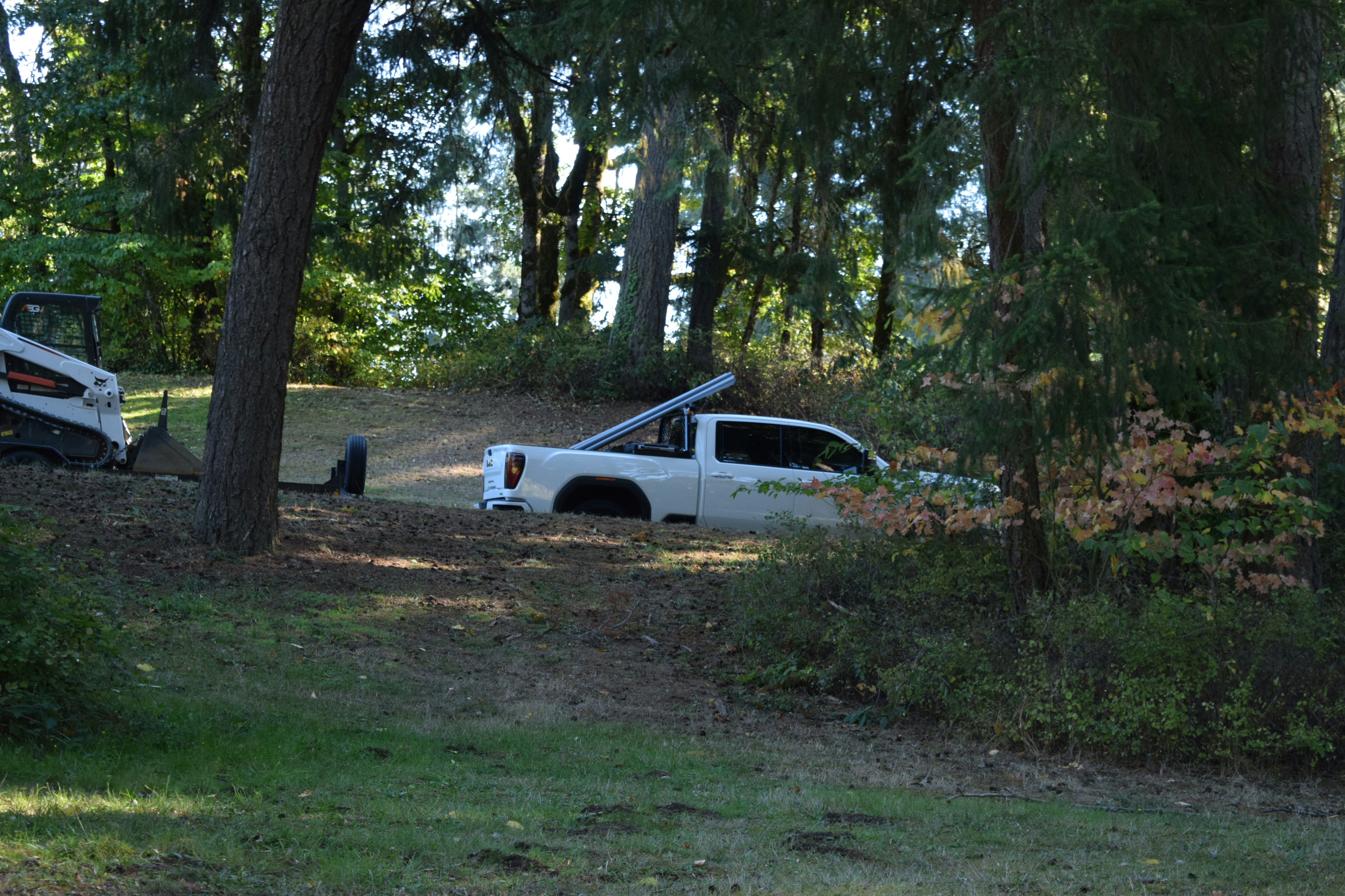 White truck stuck in dirt with bobcat nearby