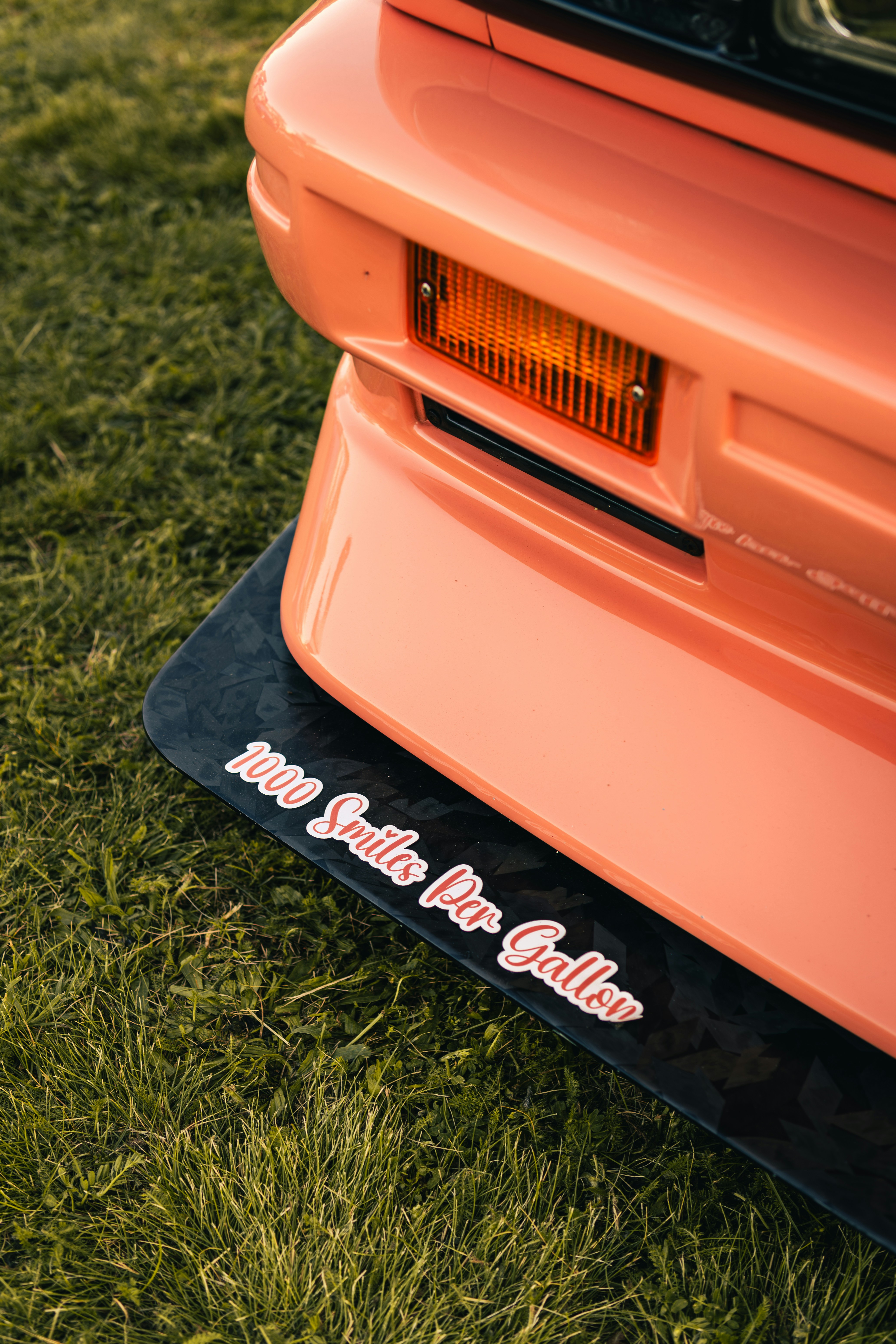 芝生にステッカーを貼ったオレンジ色の車のバンパー