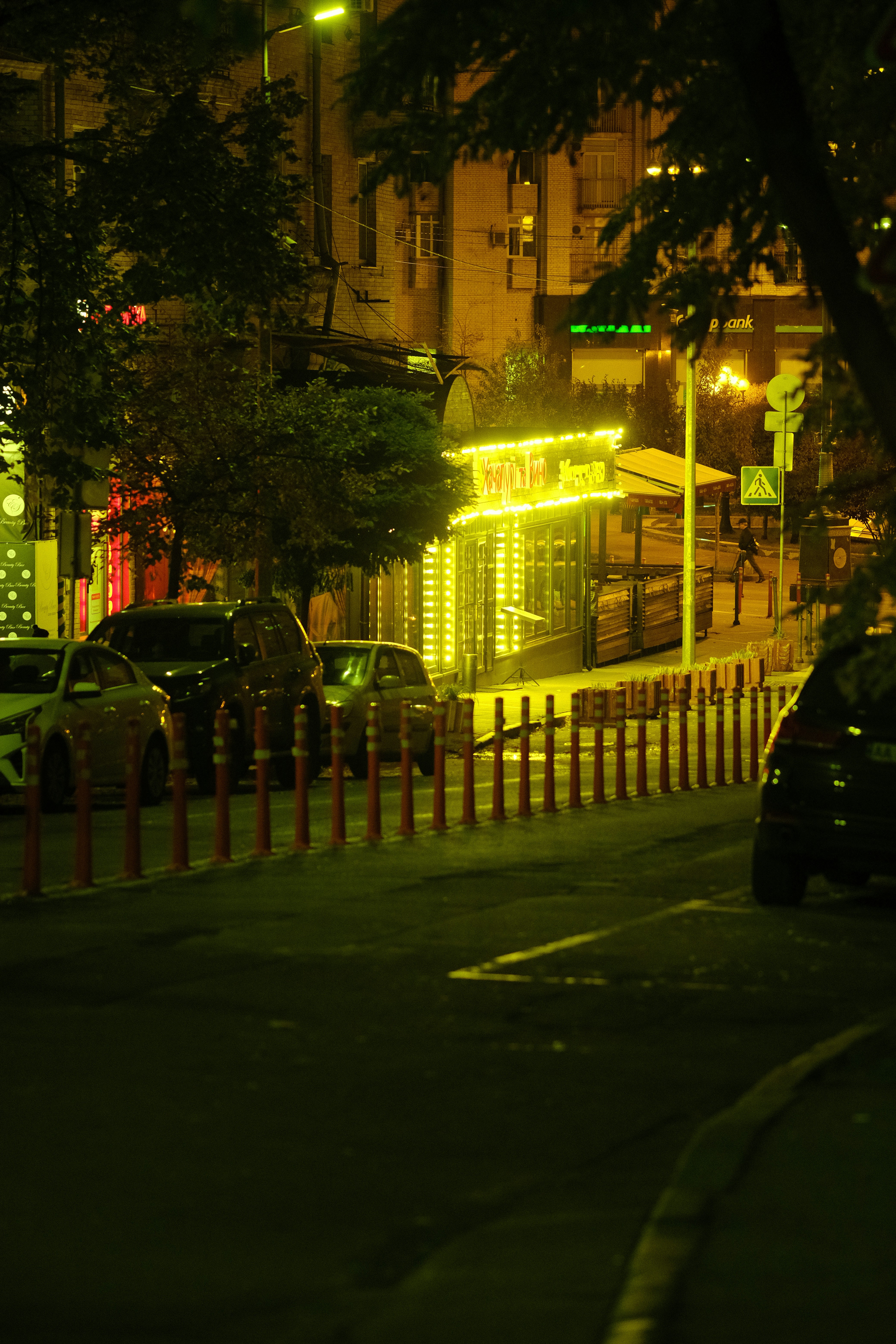 Street scene at night with illuminated kiosk and cars.