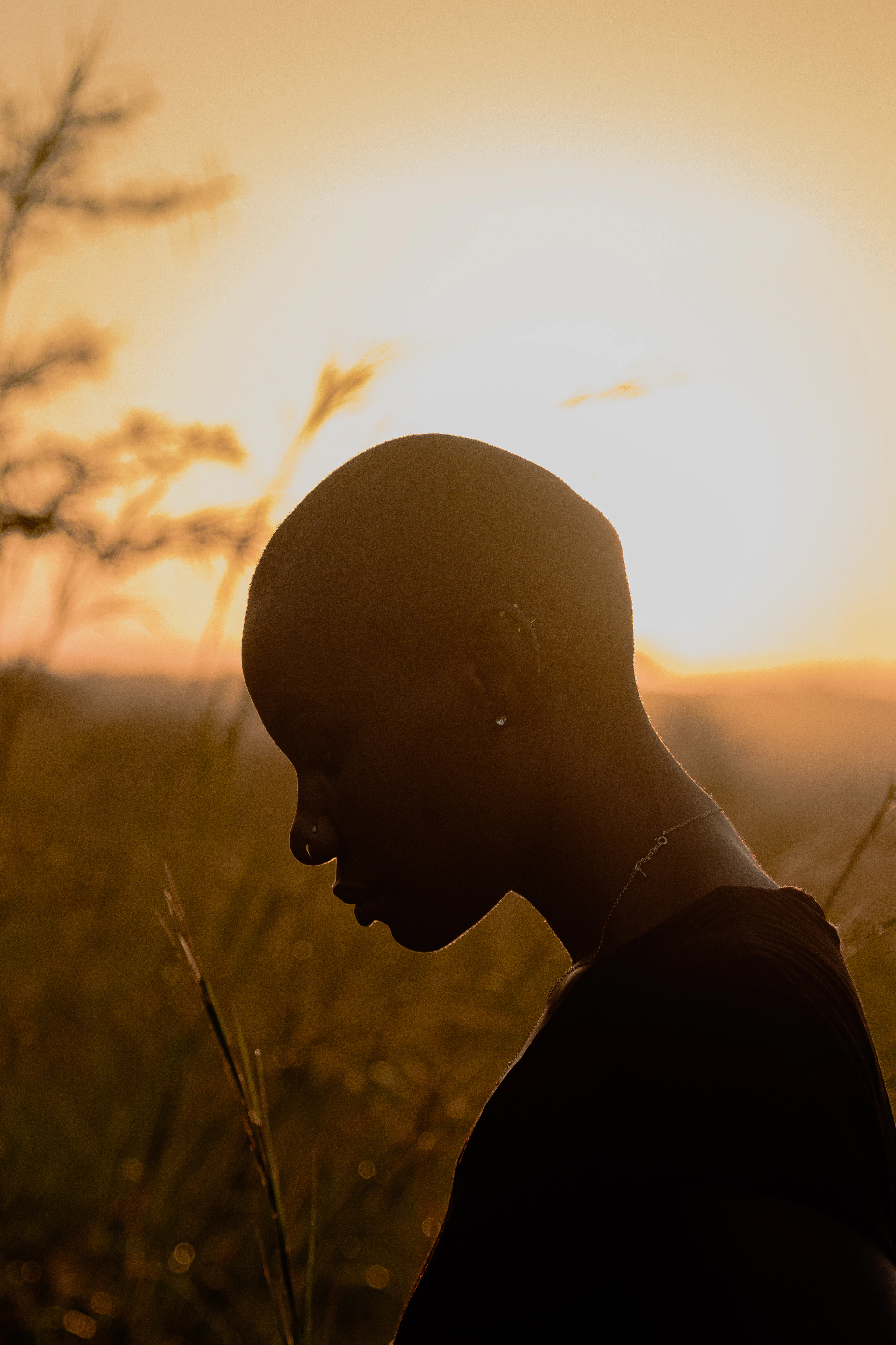 A woman in silhouette against a golden sunset, head bowed in thought