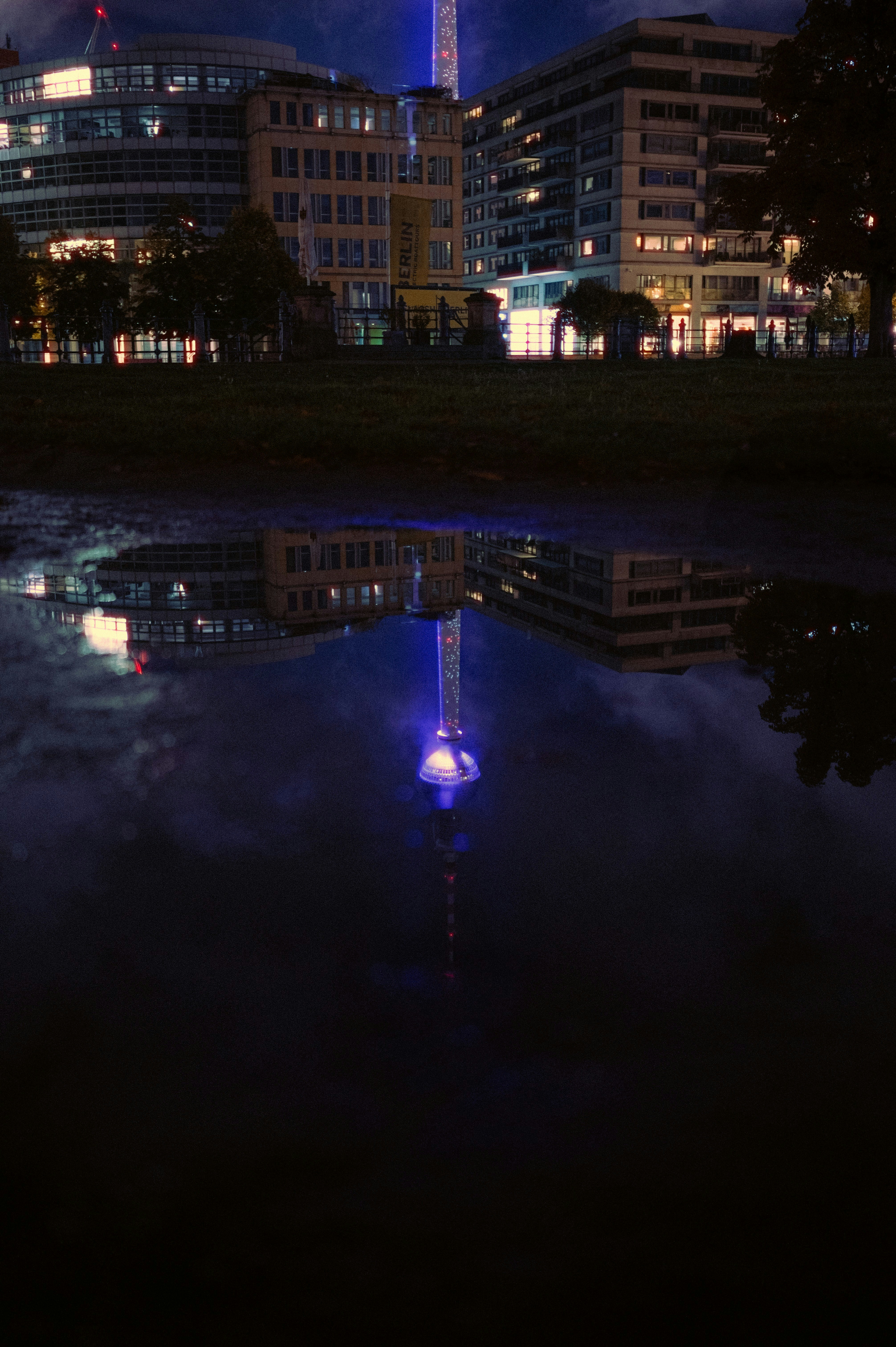 City buildings reflected in a dark puddle at night.