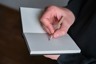 Hand holding pencil writing in a notebook.