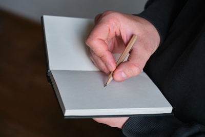 Hand holding pencil writing in a notebook.
