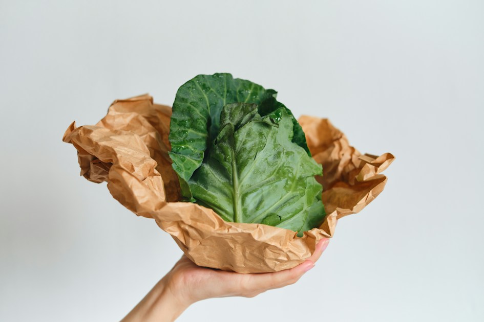 A hand holding a green leafy vegetable in brown paper