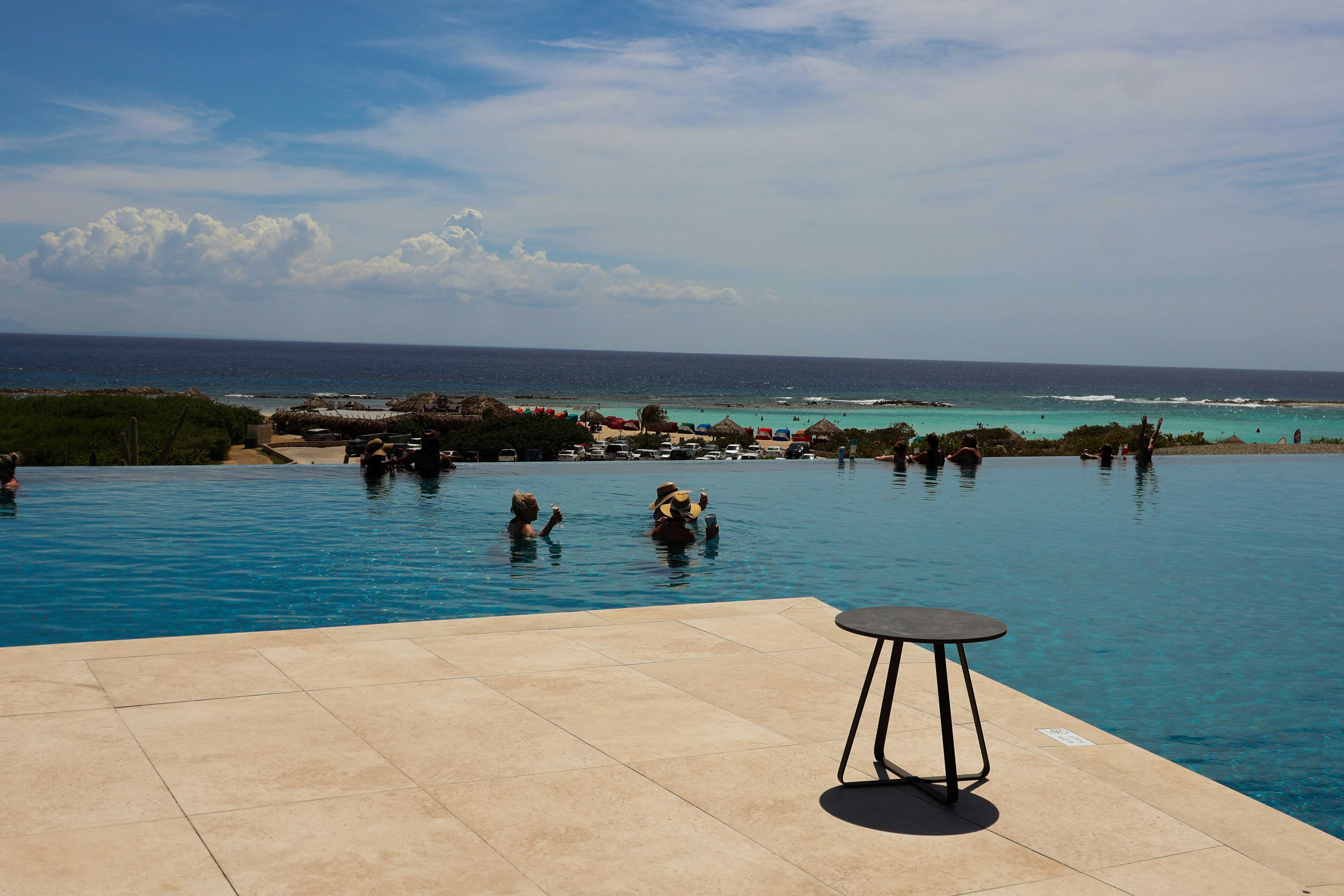 People swimming in an infinity pool overlooking the ocean.