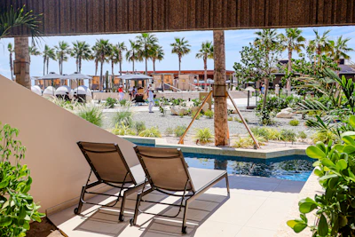 Two lounge chairs by a small pool with palm trees.