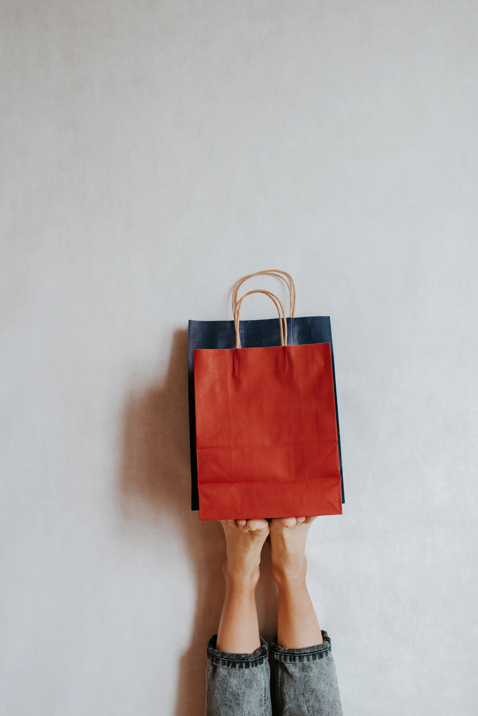Hands holding shopping bags against a wall